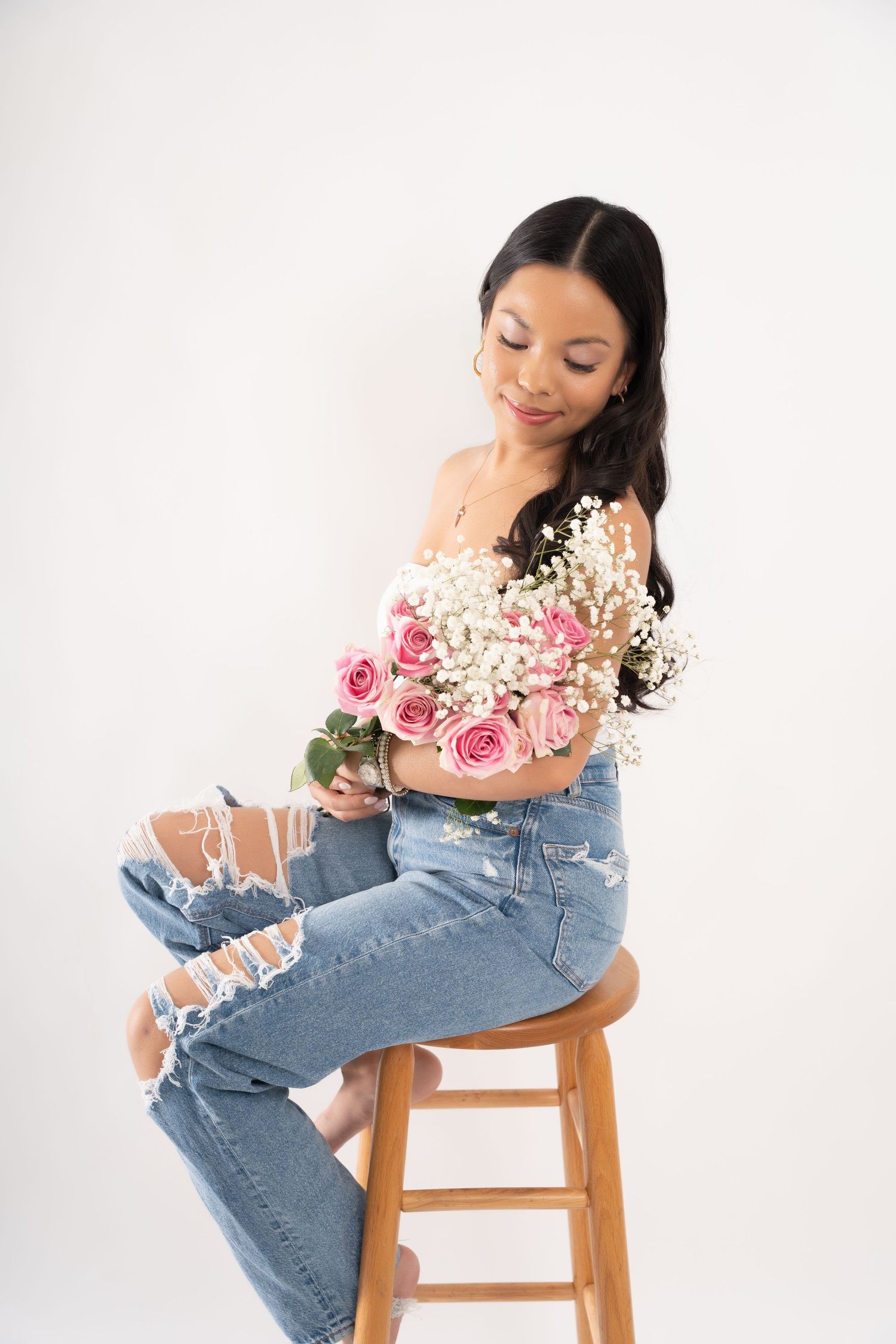 a woman poses with a bouquet of flowers on a white backdrop.