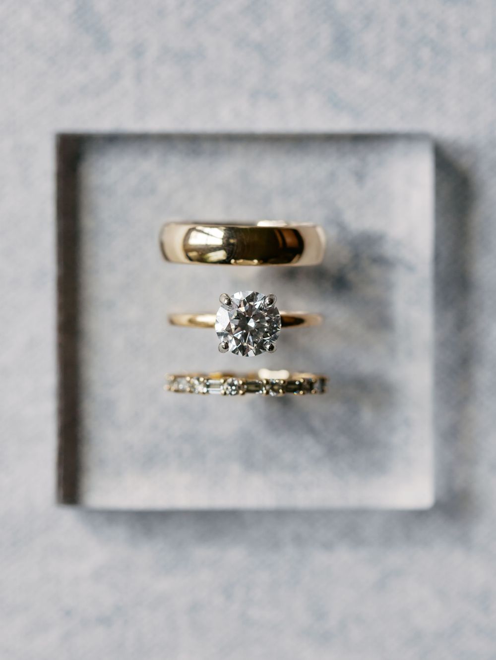 Three gold wedding rings displayed in a velvet box, featuring a diamond solitaire engagement ring flanked by two bands.
