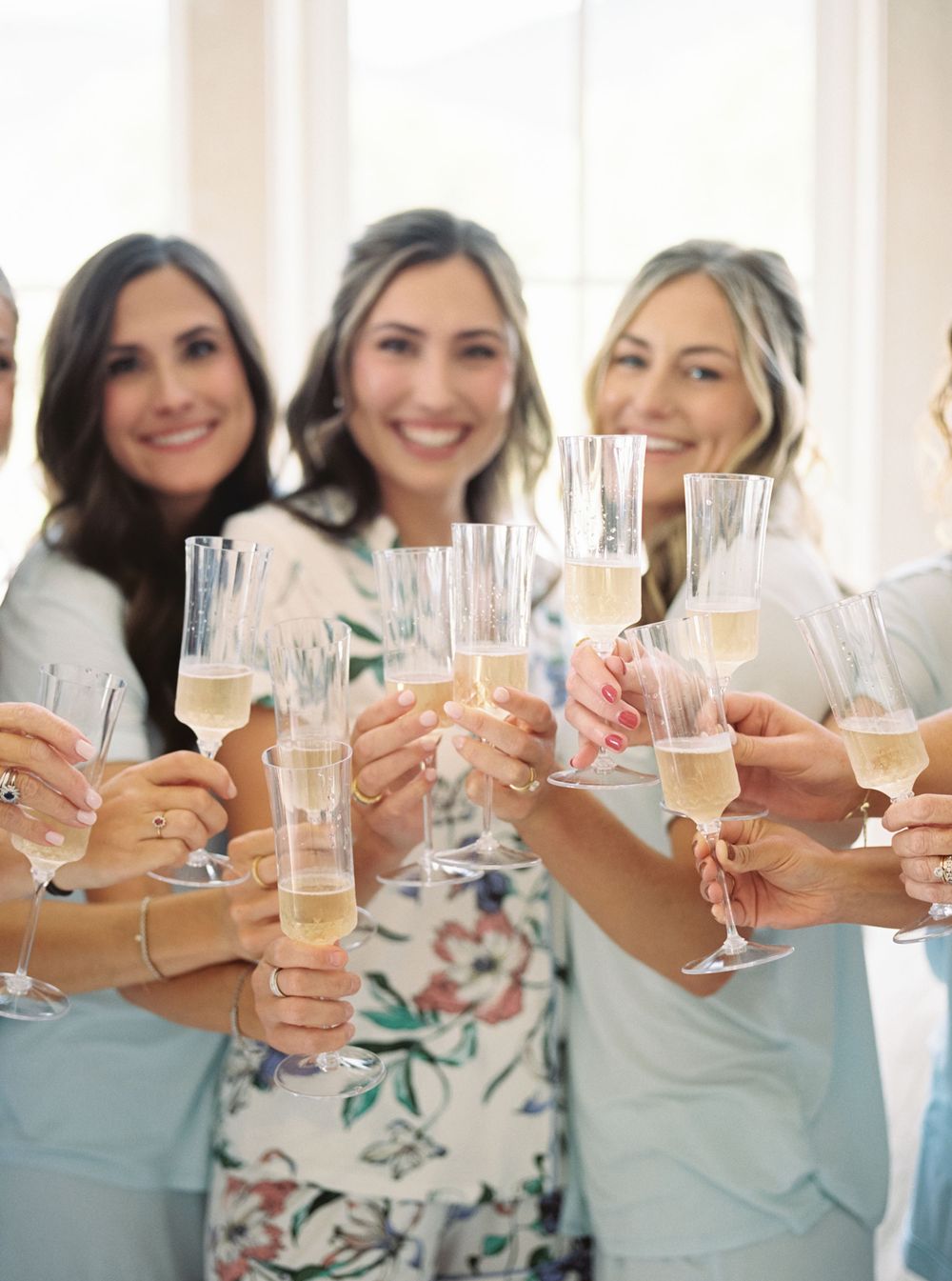 Smiling bridesmaids in robes raising champagne flutes in a celebratory toast during bridal preparations.