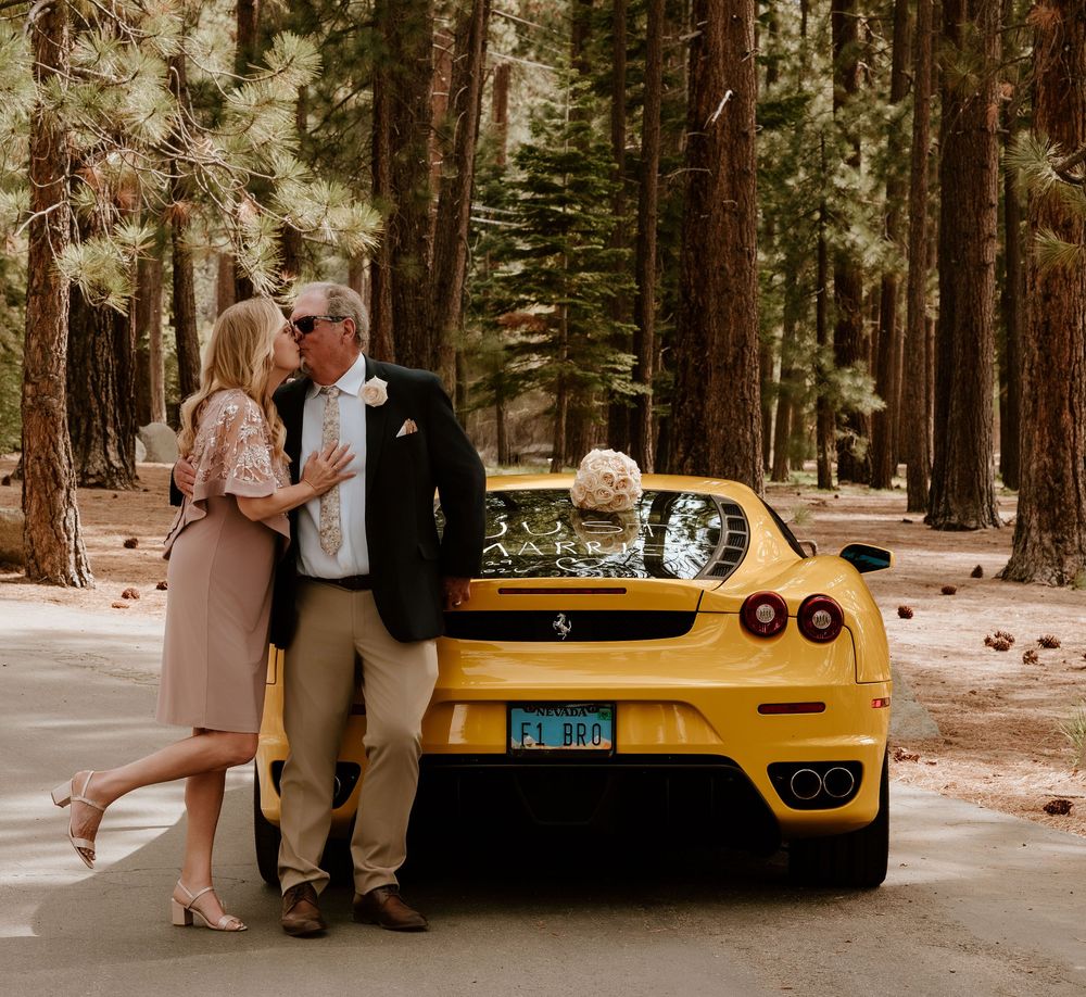 Couple embracing beside a yellow Ferrari sports car surrounded by tall pine trees in a forest setting.