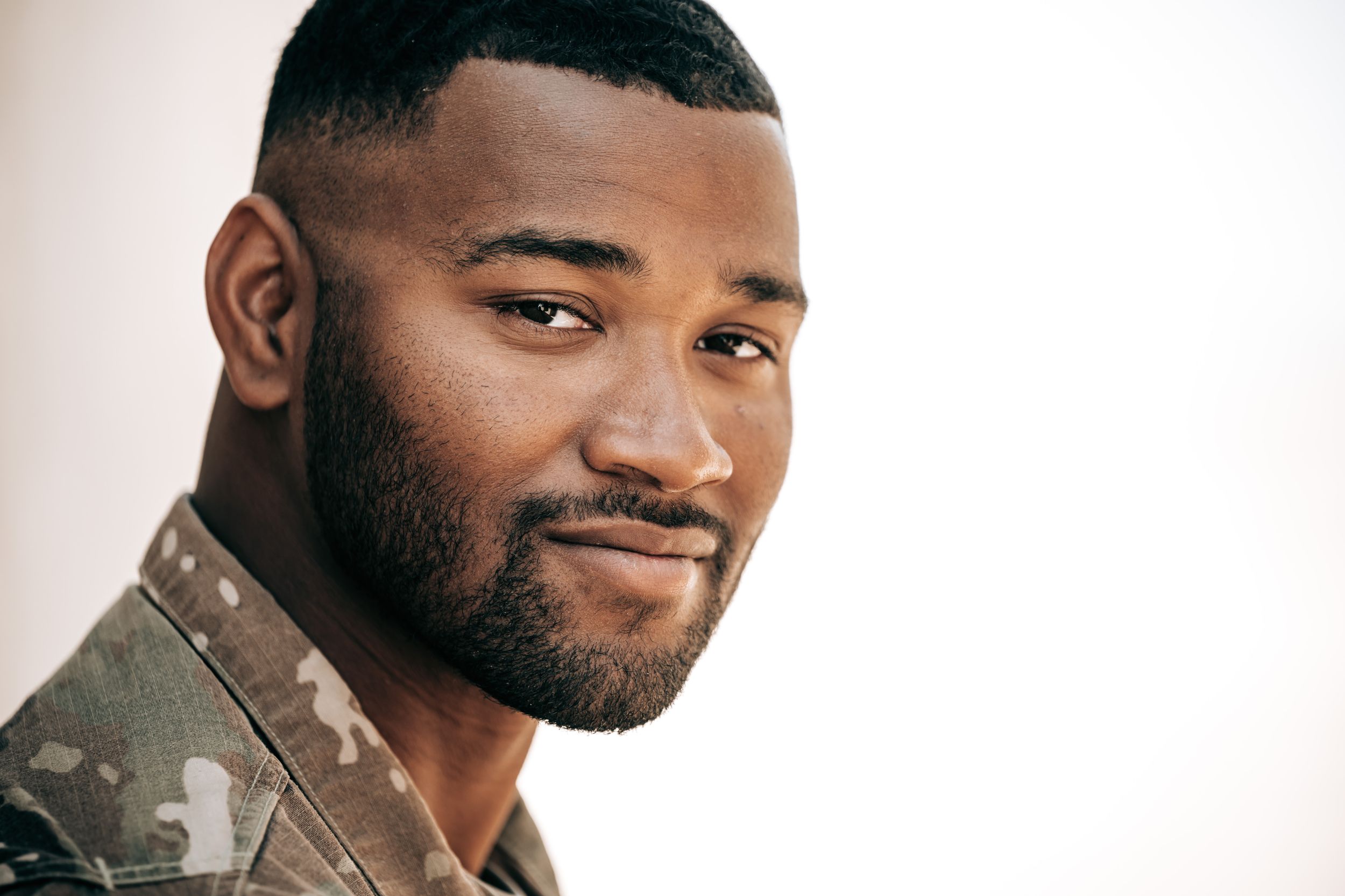 Close-up portrait of a confident young man with a beard wearing a camo jacket.