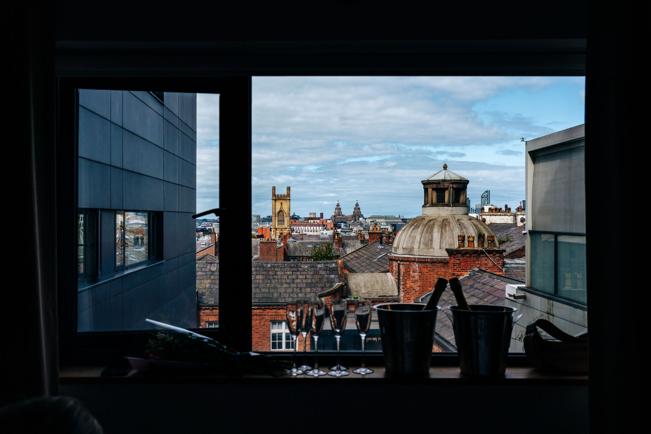 Liverpool City rooftop view through hotel window showing historic church spires and Victorian architecture on a cloudy day.