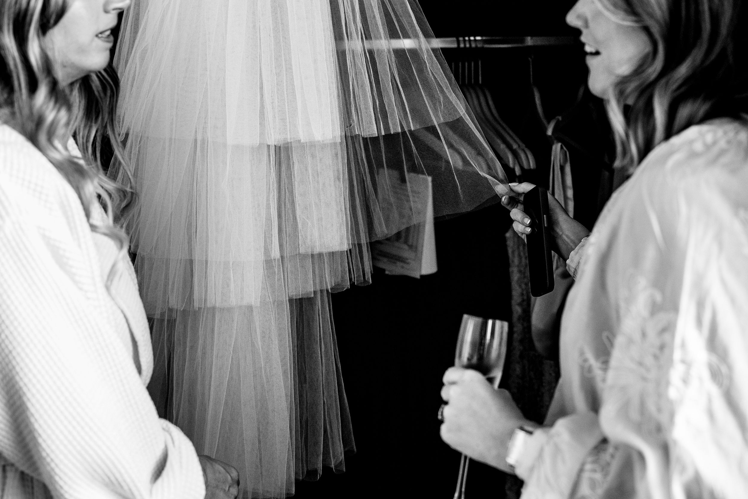 Black and white close-up of bride and bridesmaid examining wedding veil while holding champagne glass at Hope street Hotel.