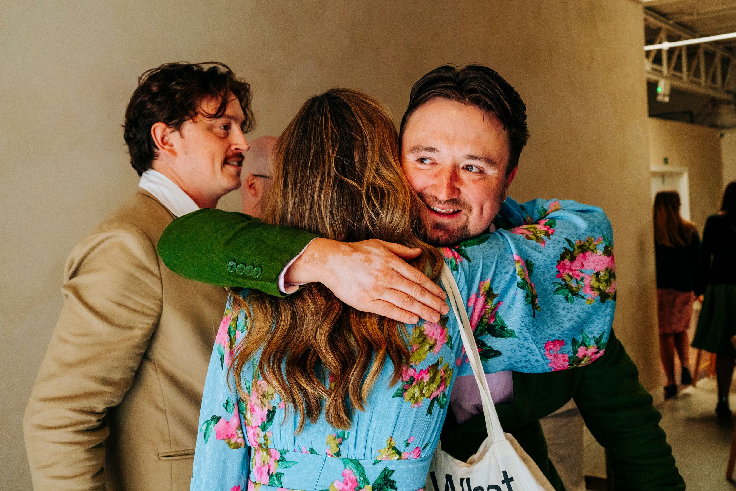 Two guests in floral outfits share a warm embrace at a wedding reception.