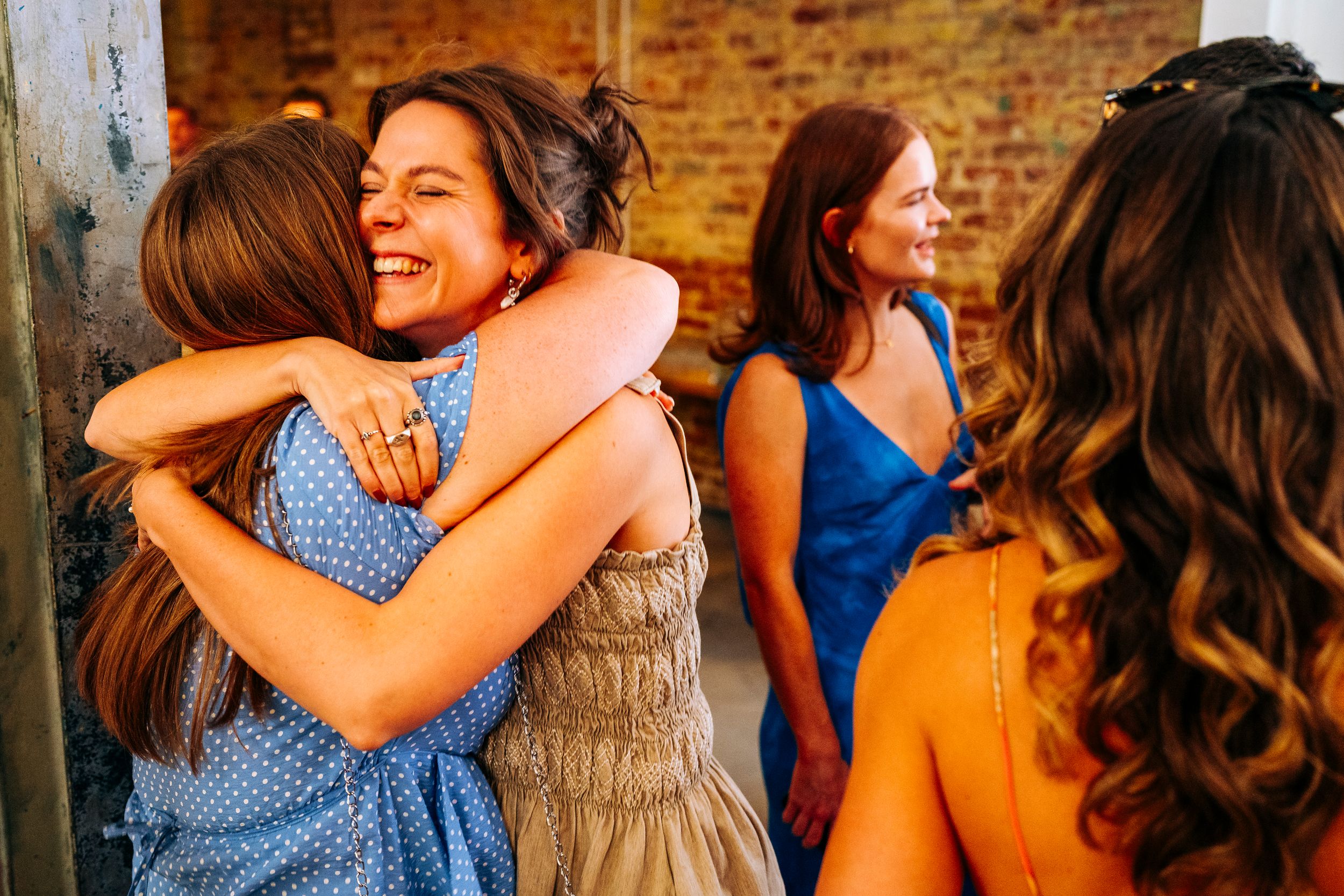 Two women share a joyful hug at a wedding celebration outdoors.