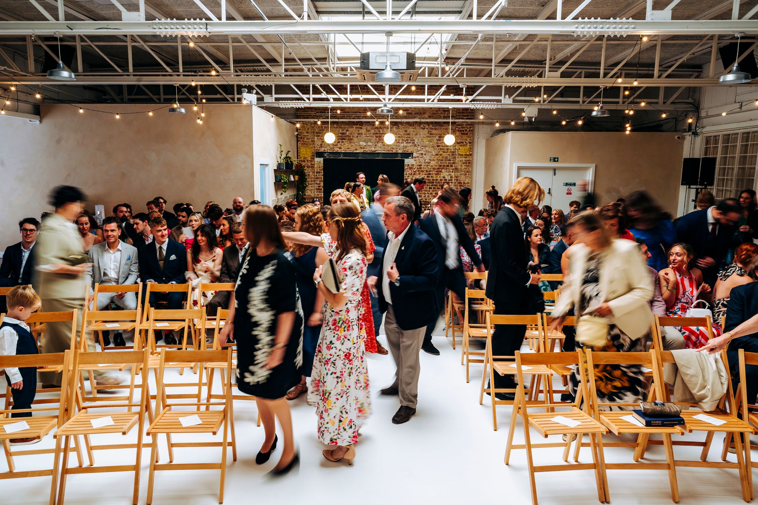 Wedding guests move through a modern industrial ceremony venue with white aisle.