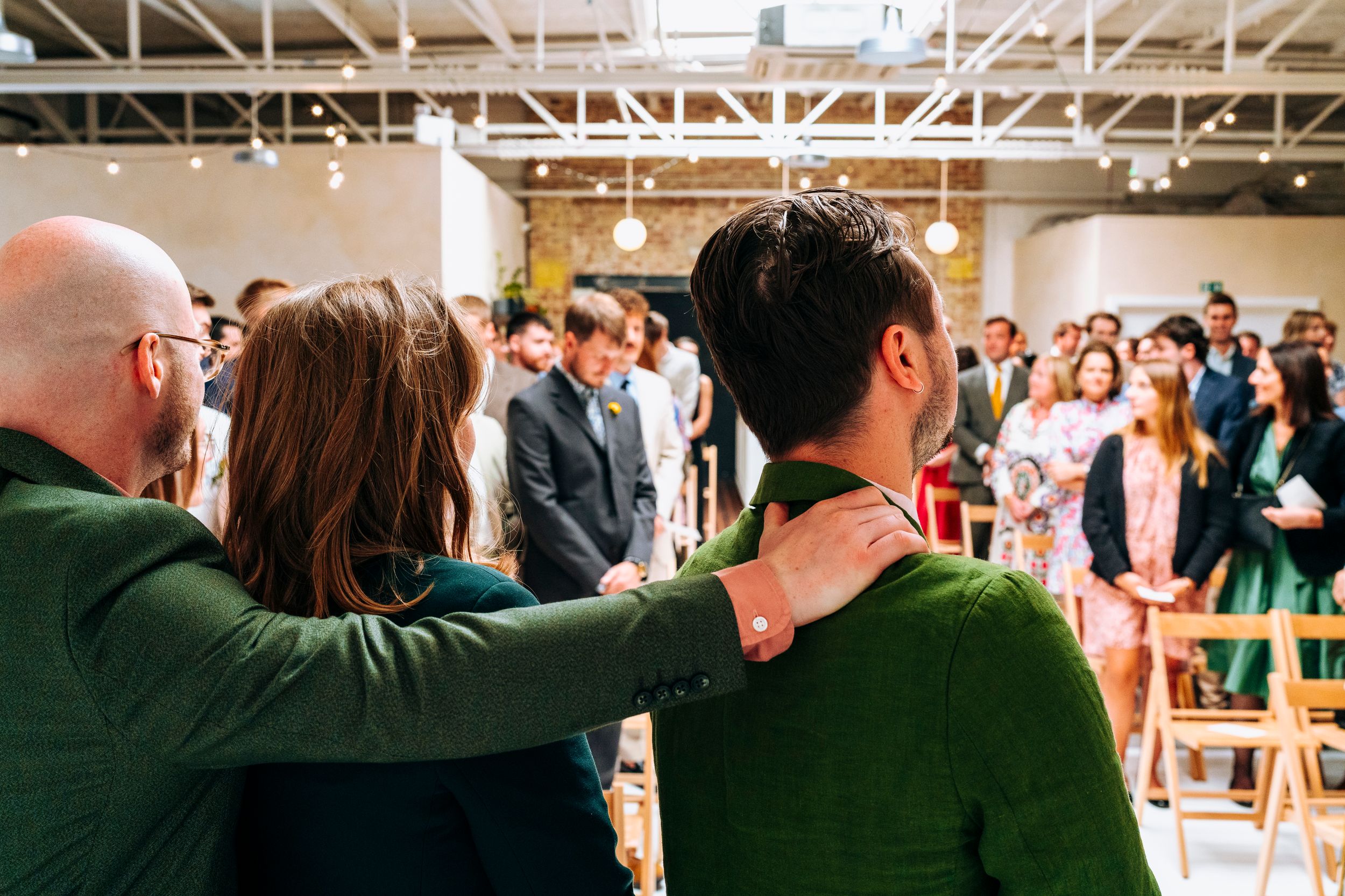 Wedding guests watch ceremony from behind in a modern white venue space.