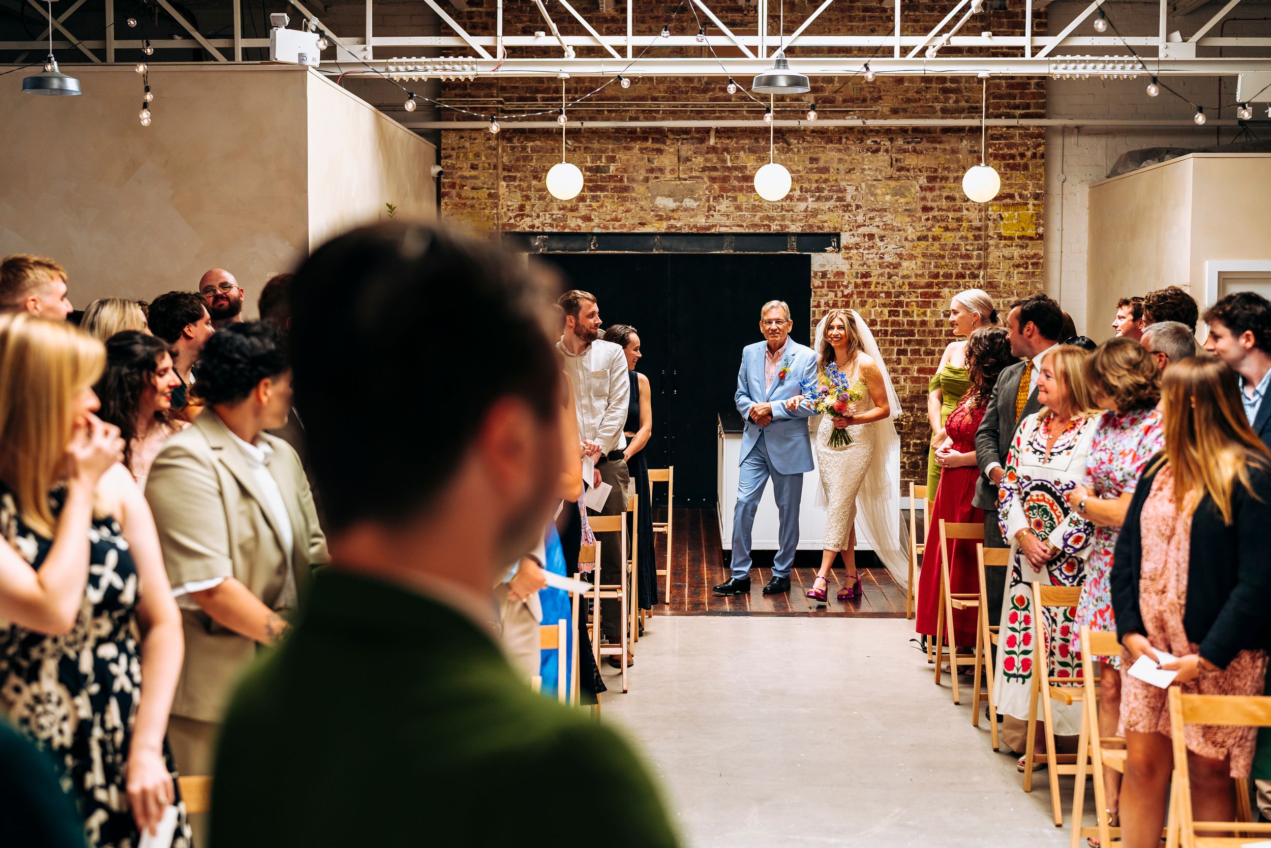Couple walks down the aisle in a bright industrial wedding ceremony space.