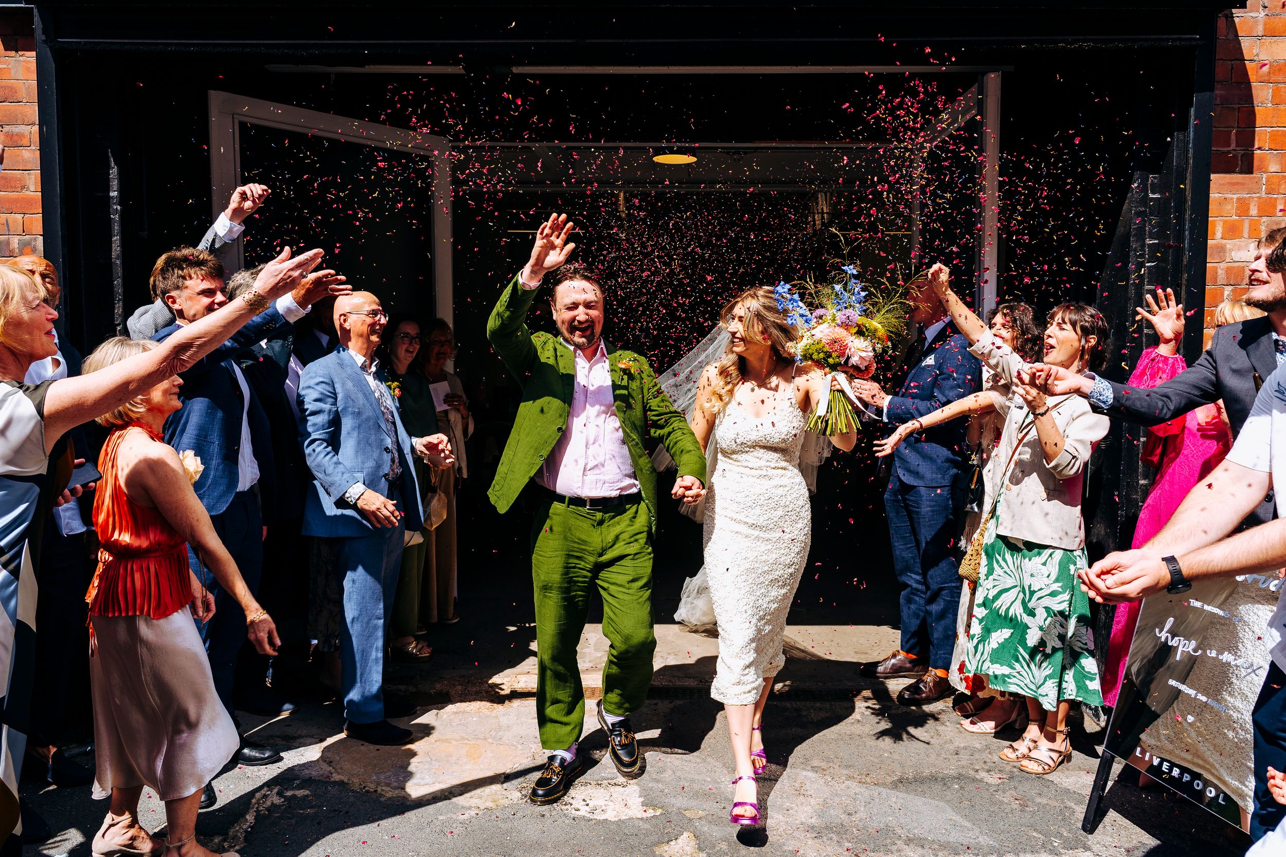 Joyful bride and groom exit wedding venue as guests throw colorful confetti in celebration.