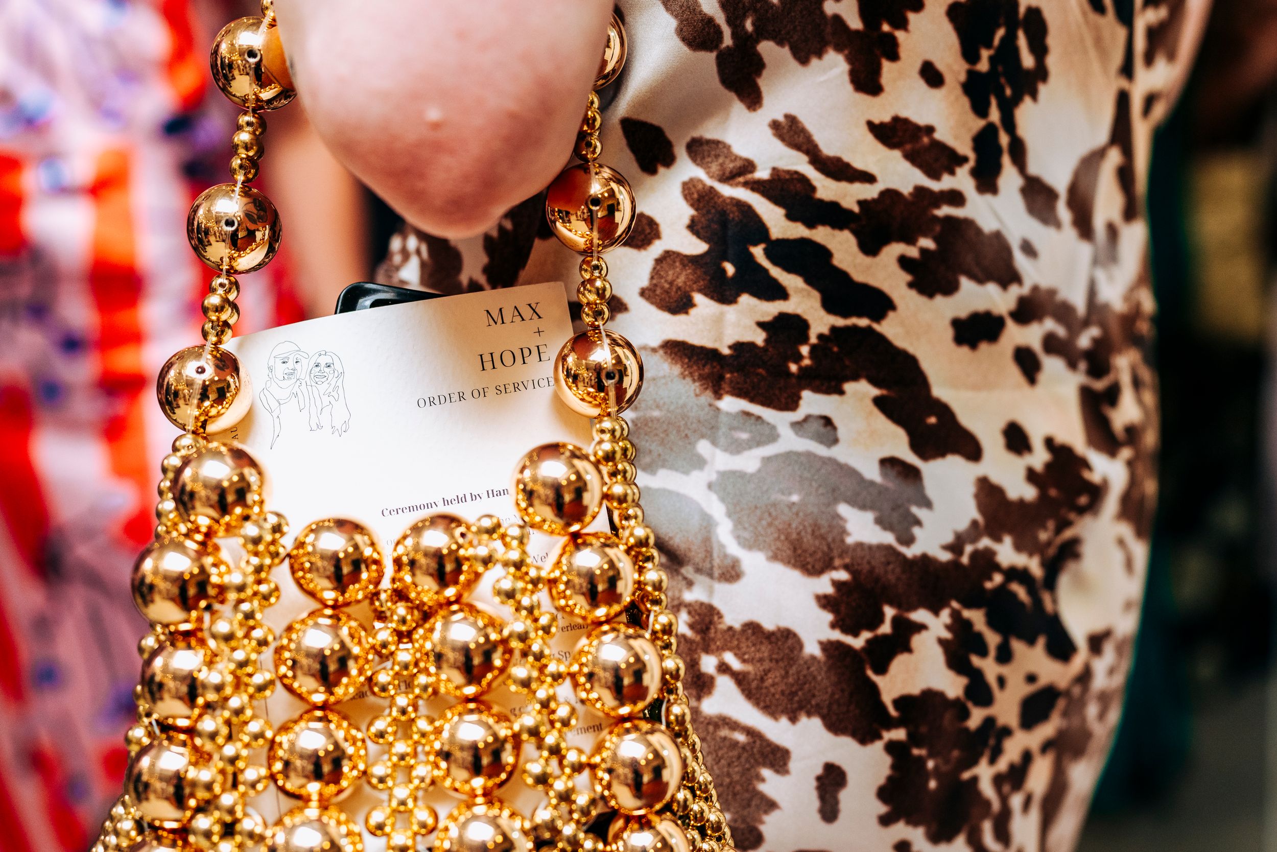 Close-up of a gold beaded ball chain handbag with Max Mara label against leopard print fabric.