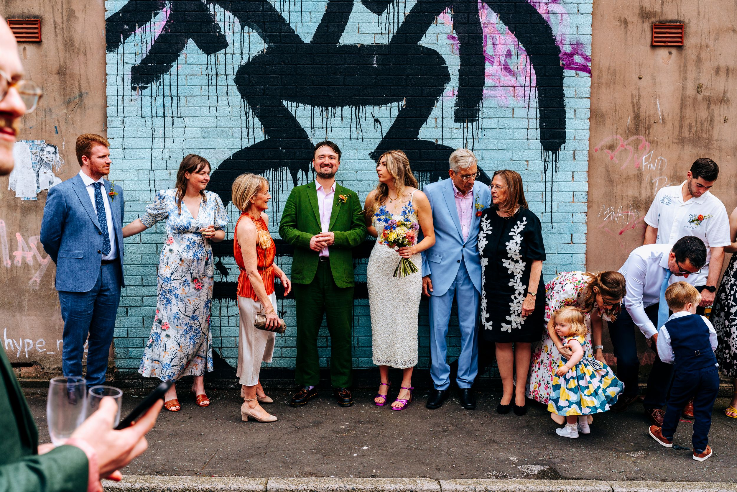 Wedding party group photo in front of a colorful graffiti wall with bride holding flowers.