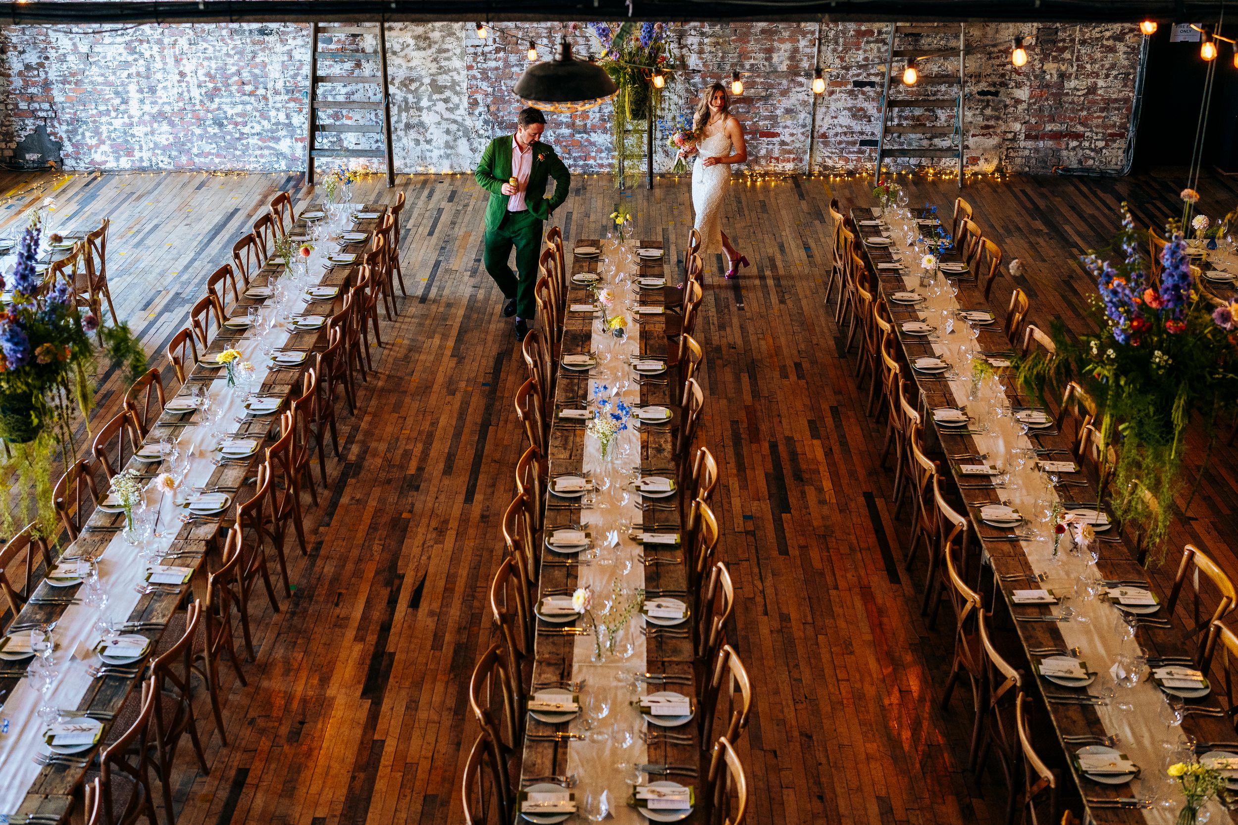 Aerial view of elegantly set long banquet tables in a rustic industrial wedding reception venue.