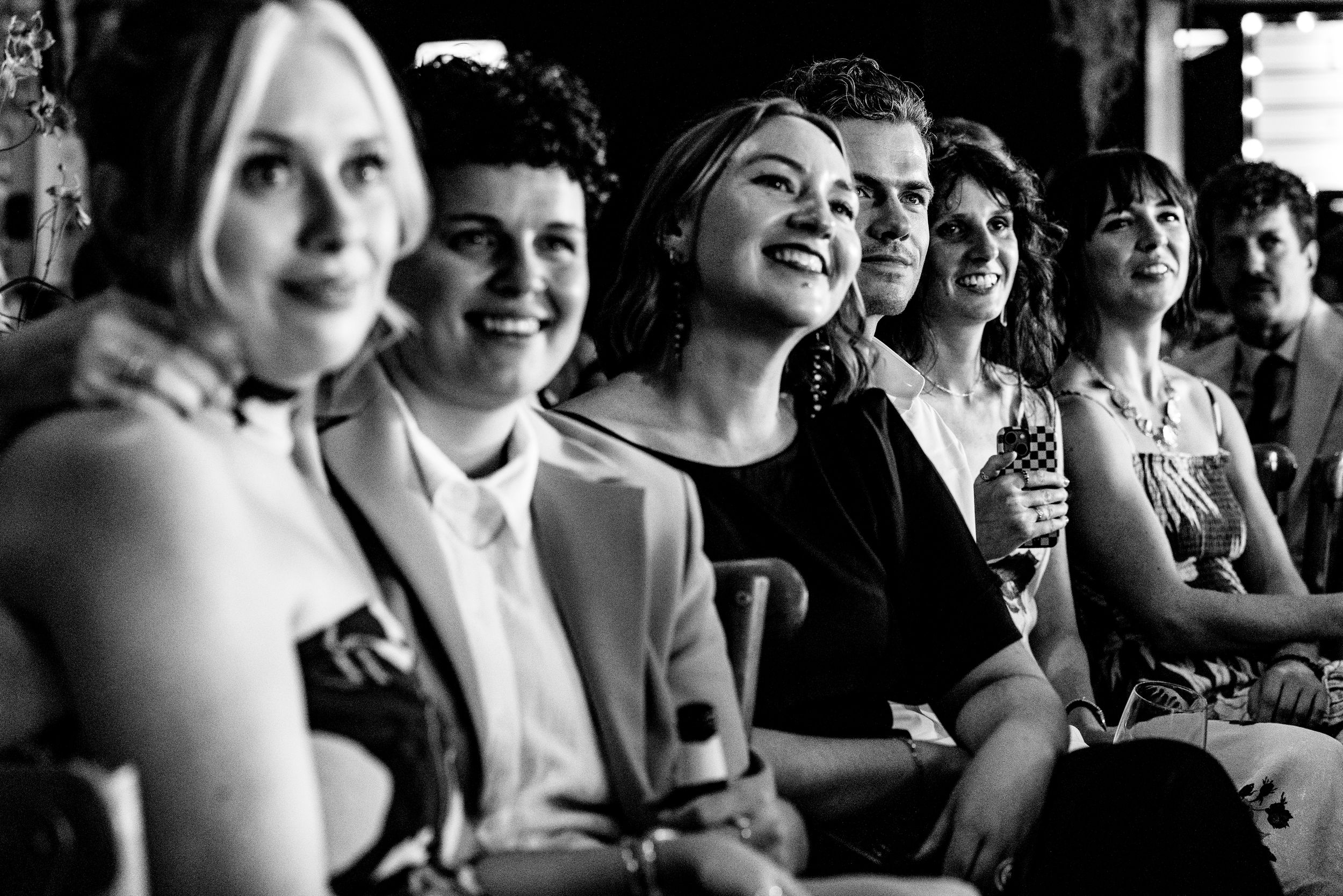 Black and white photo of smiling women seated together enjoying a wedding ceremony.