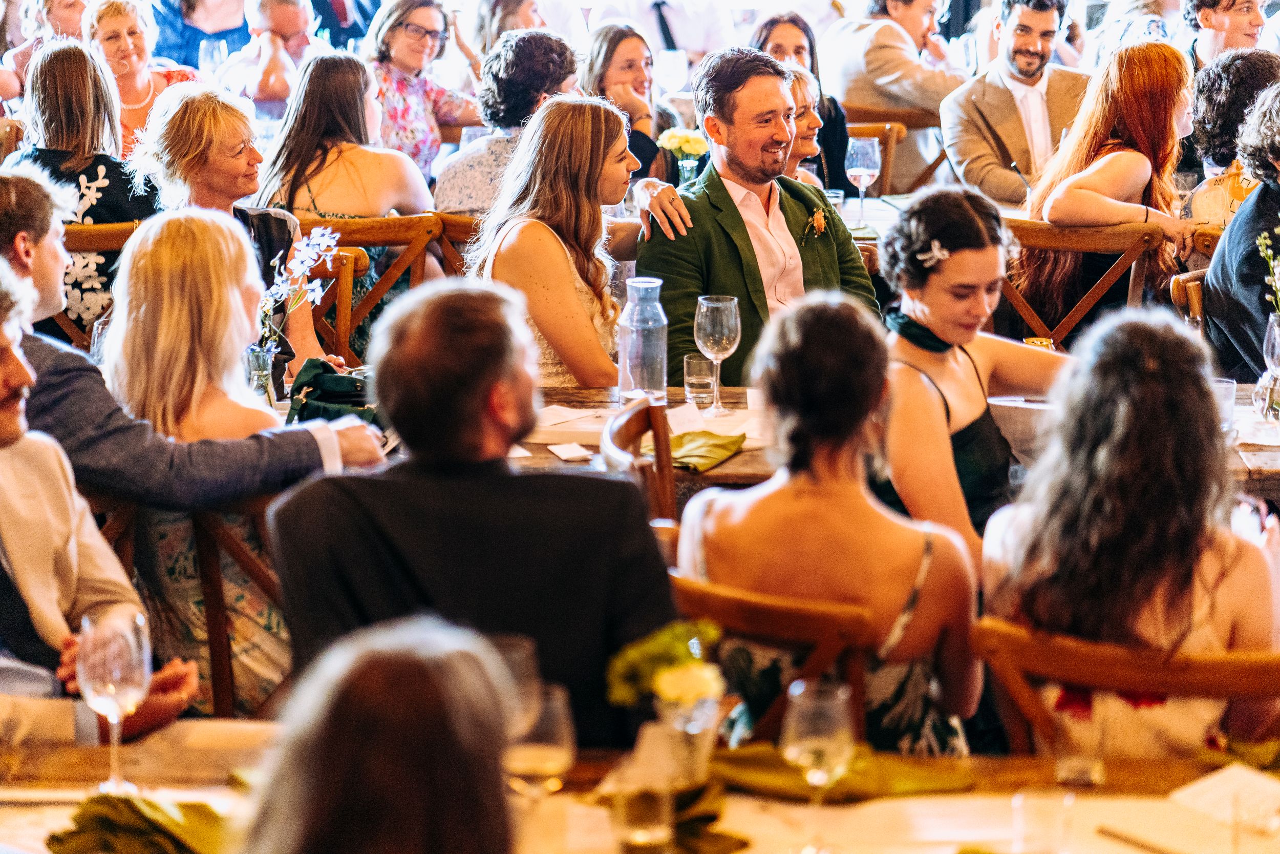 Cheerful wedding guest in green jacket laughing with guests at a crowded reception dinner.