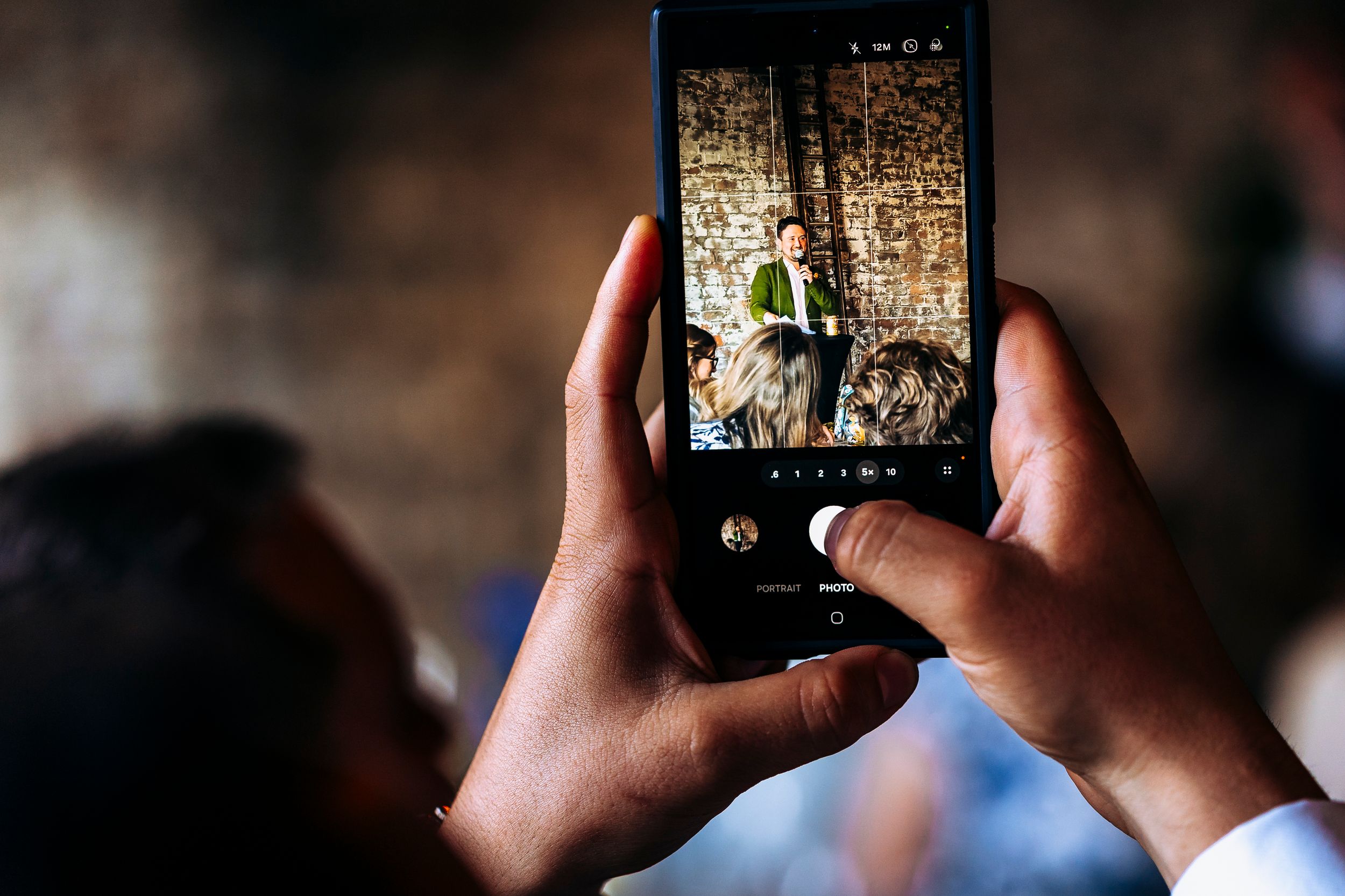 Close-up of hands holding a smartphone photographing a man on stage at an event.