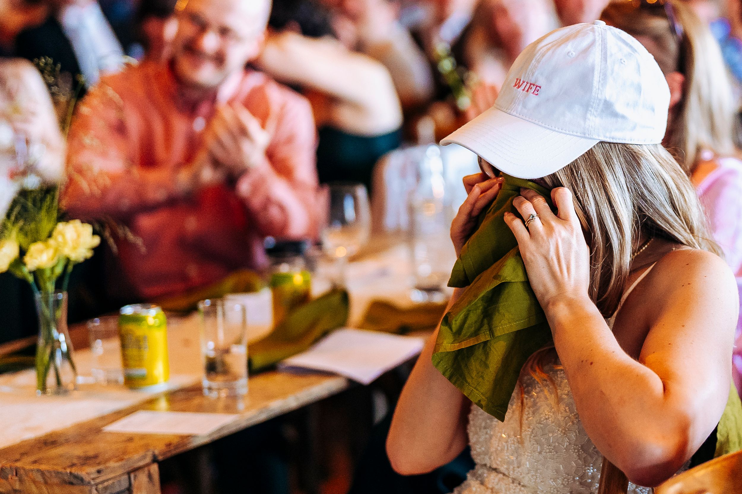 Emotional Bride in in white cap wiping tears with a green napkin at reception.