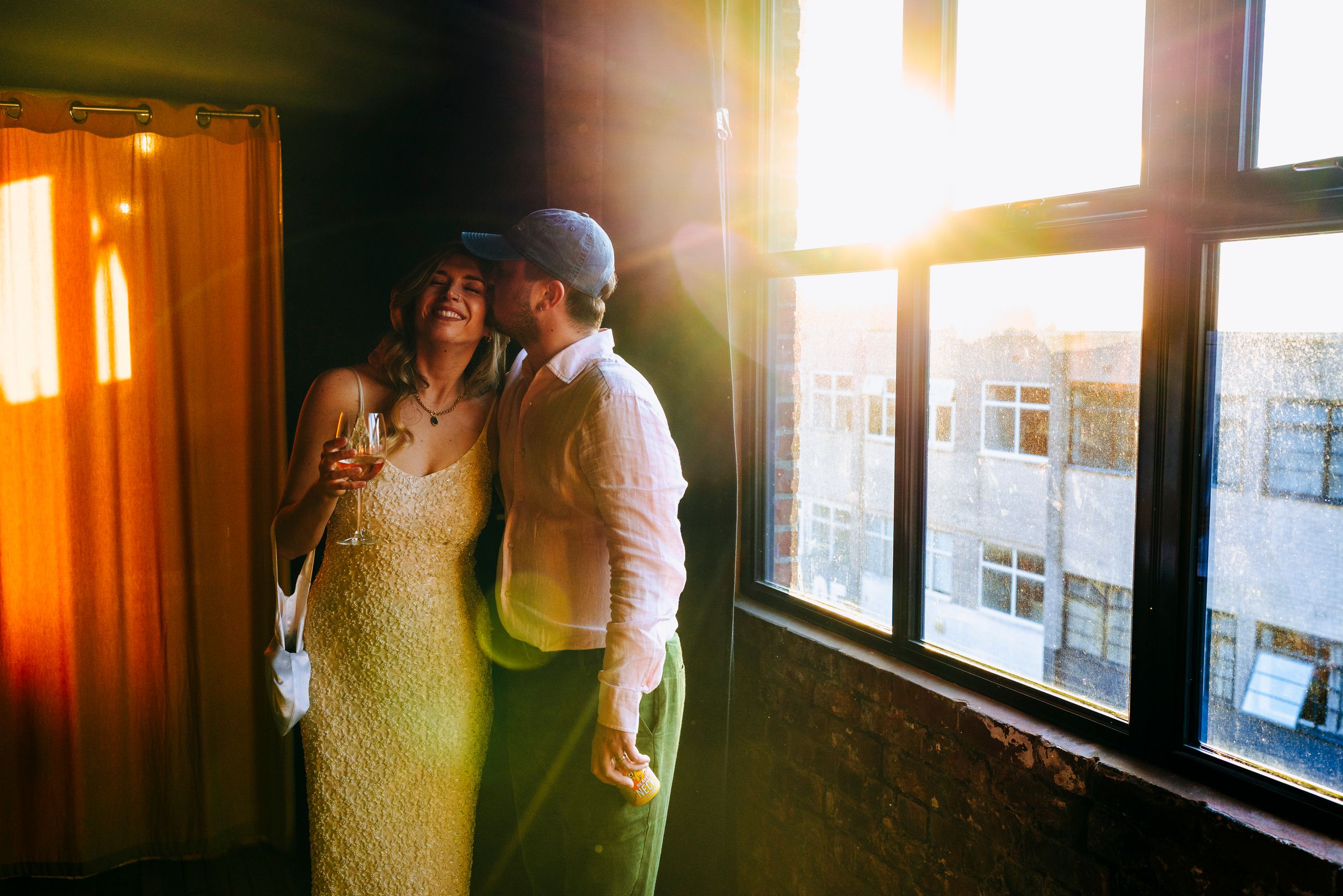Couple sharing a romantic moment bathed in golden sunset light by large warehouse windows.