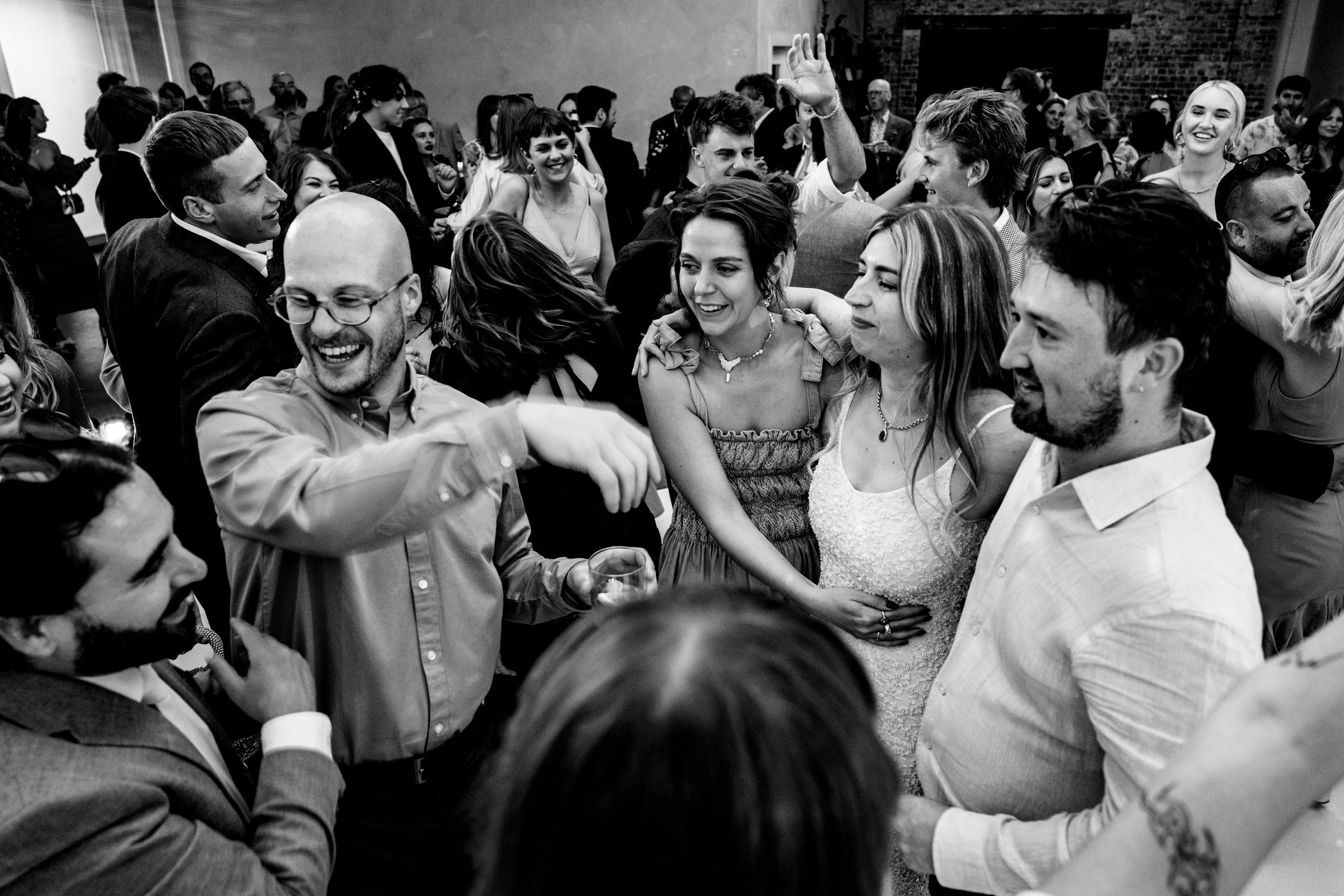 Joyful wedding guests dancing and celebrating together on the dance floor in black and white.
