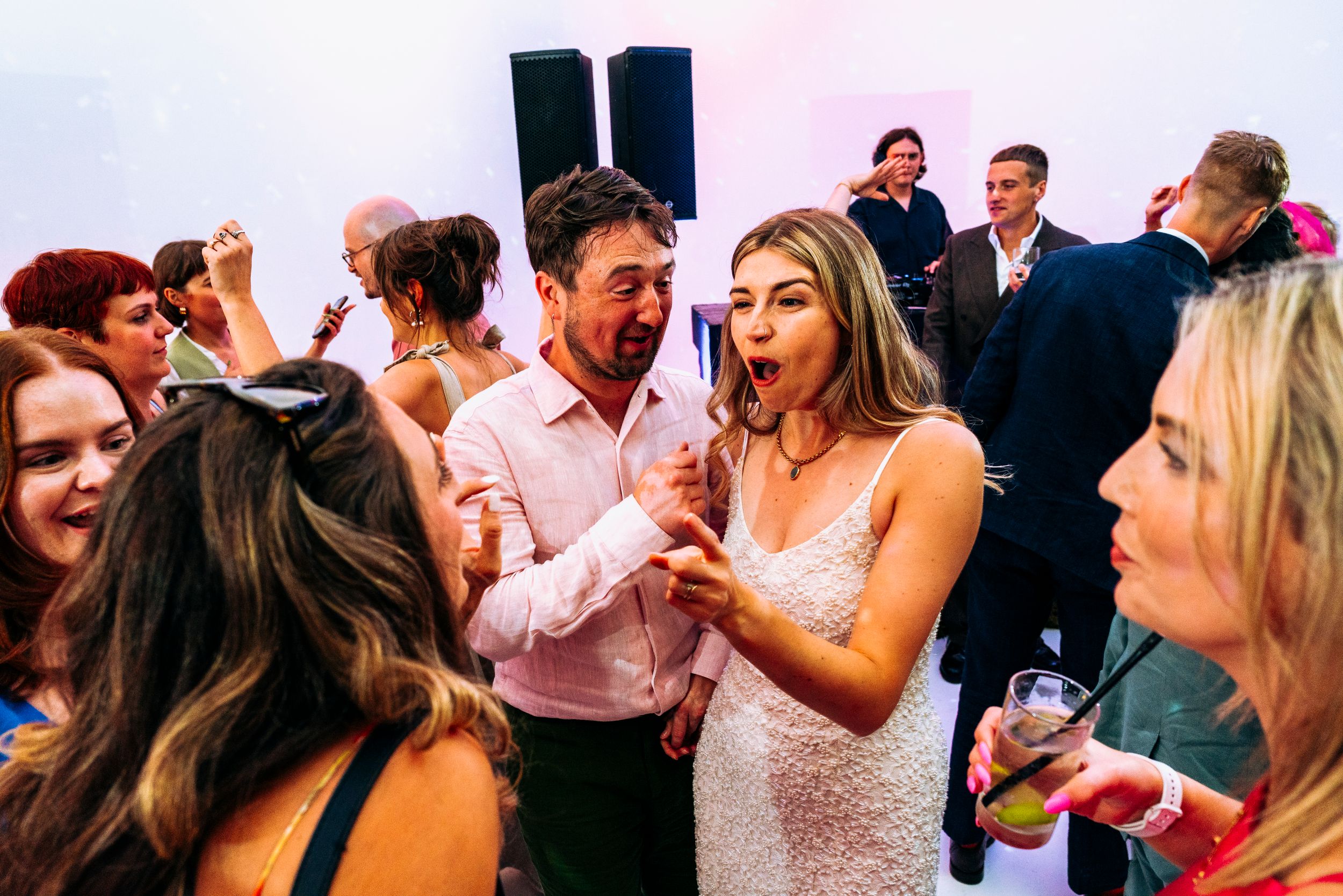 Bride in lace gown dancing energetically with guests at a lively wedding reception party.