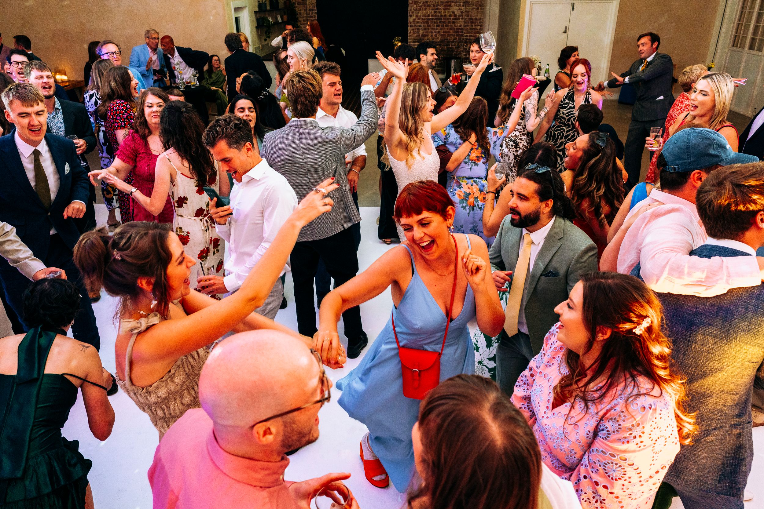 Energetic wedding guests filling the dance floor with lively dancing at a bright reception.