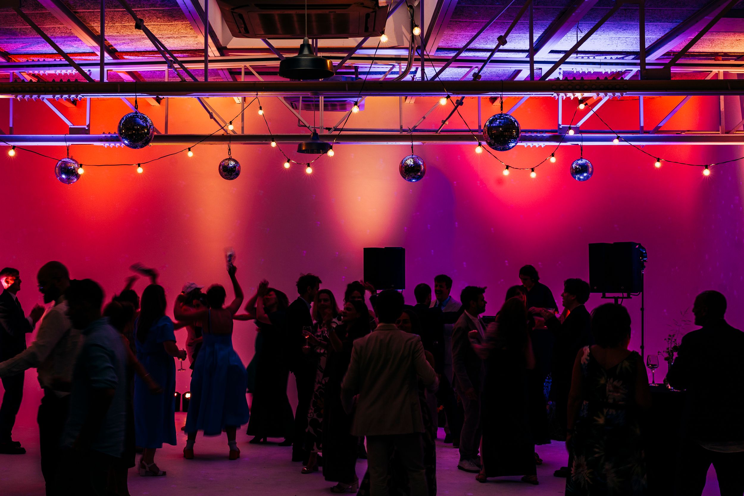 Silhouettes of wedding guests dancing under colorful purple and orange disco lights at reception.