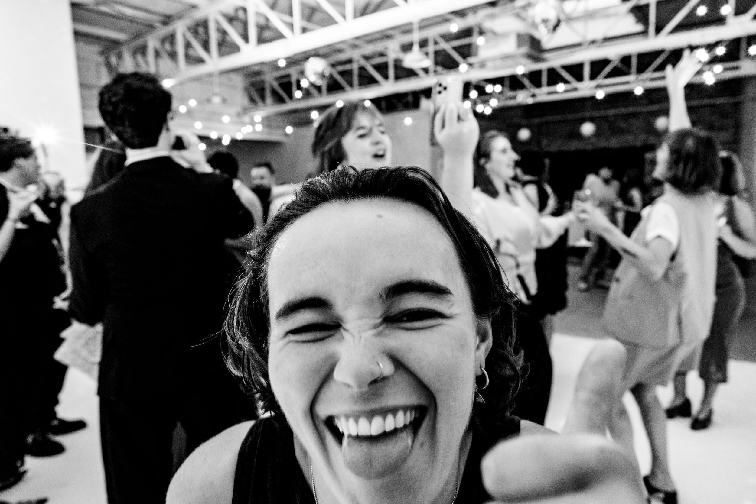 A laughing woman sticks out her tongue at the camera during a lively black and white wedding reception.
