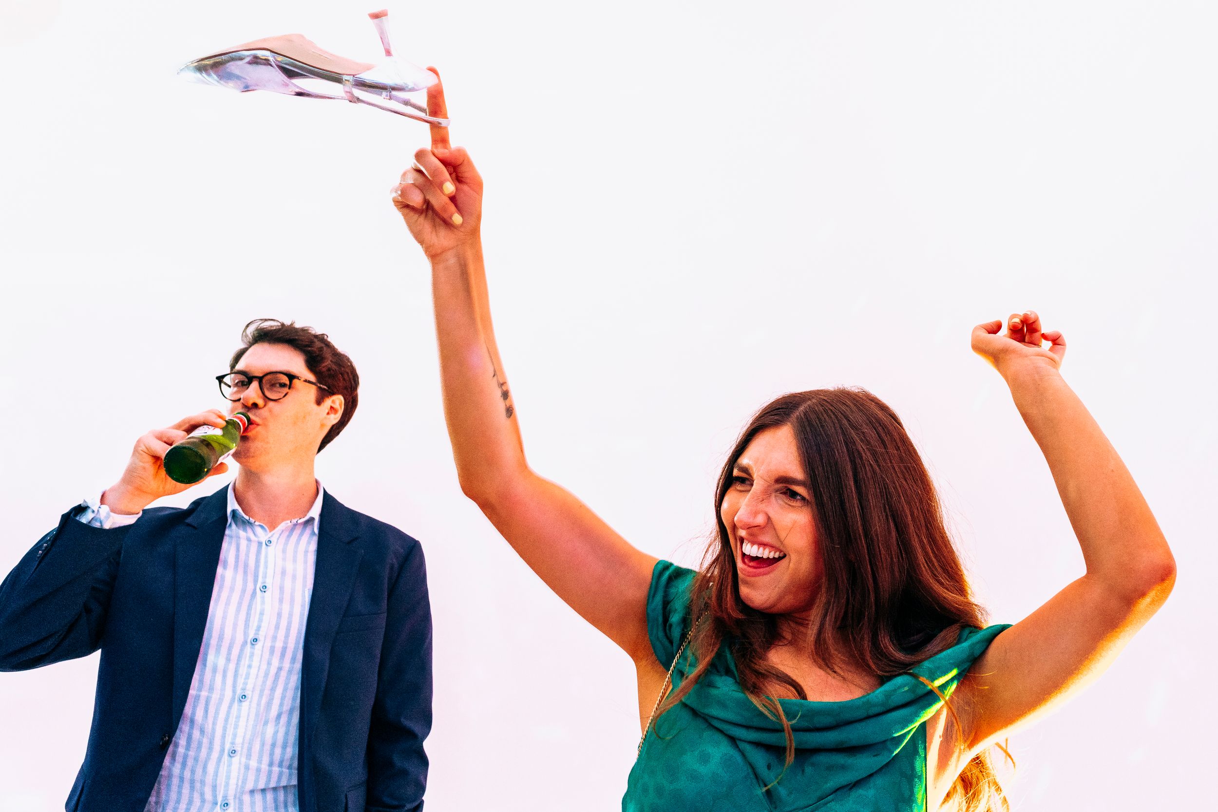 A woman joyfully holds a toy airplane aloft while a man drinks a beer bottle at an outdoor celebration.