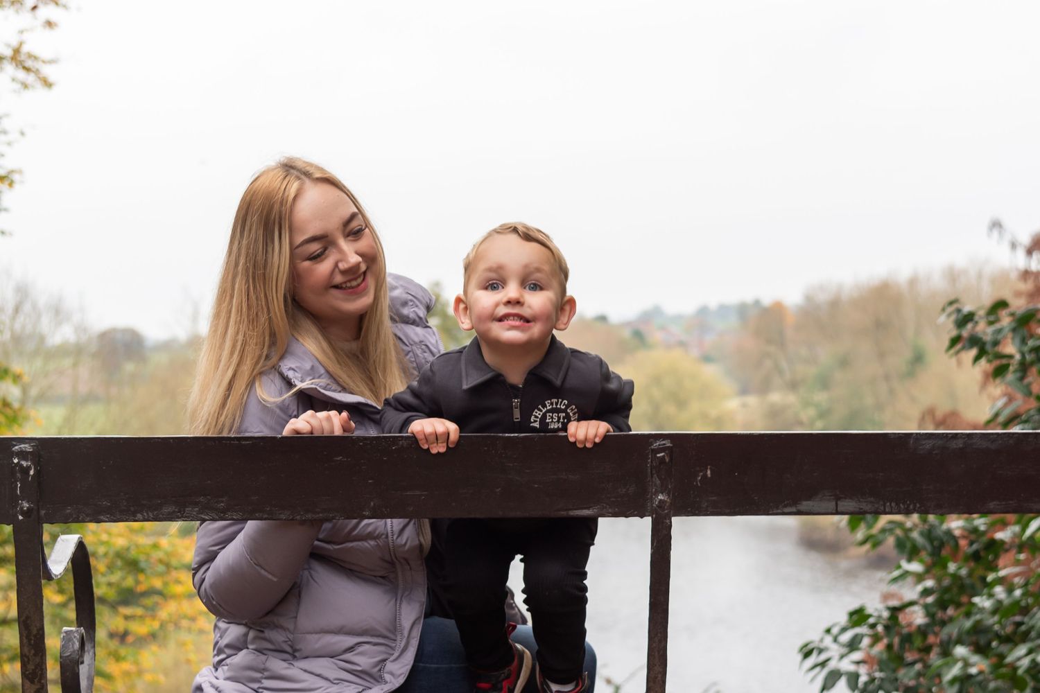 Family members sharing a moment together on a wooden fence overlooking water.
