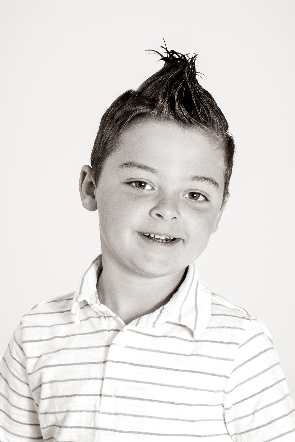 Smiling young boy with spiked hair poses for a classic black and white studio portrait photo.