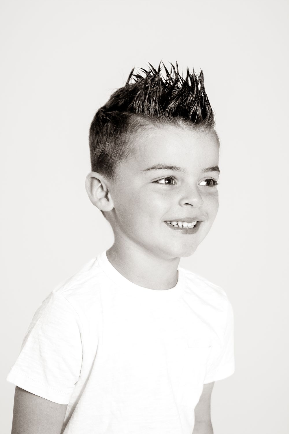 Black and white portrait of a smiling young boy with spiked hair wearing a white t-shirt.
