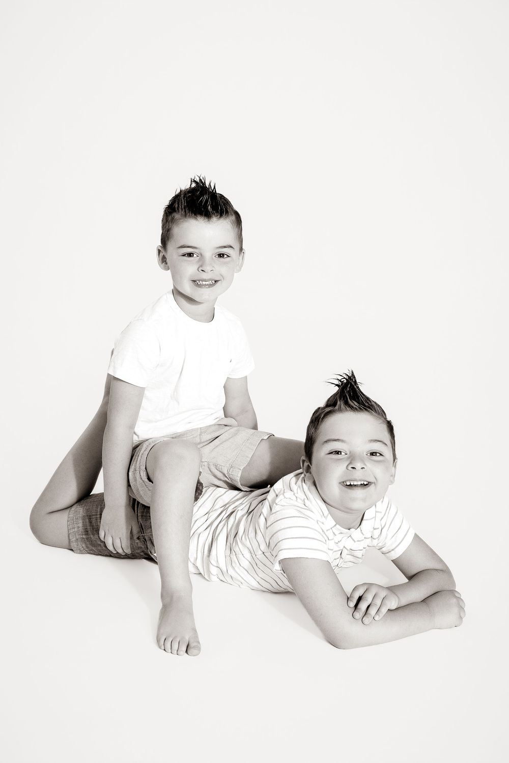 Black and white photo of two smiling boys with mohawk hairstyles posing together on a white background.