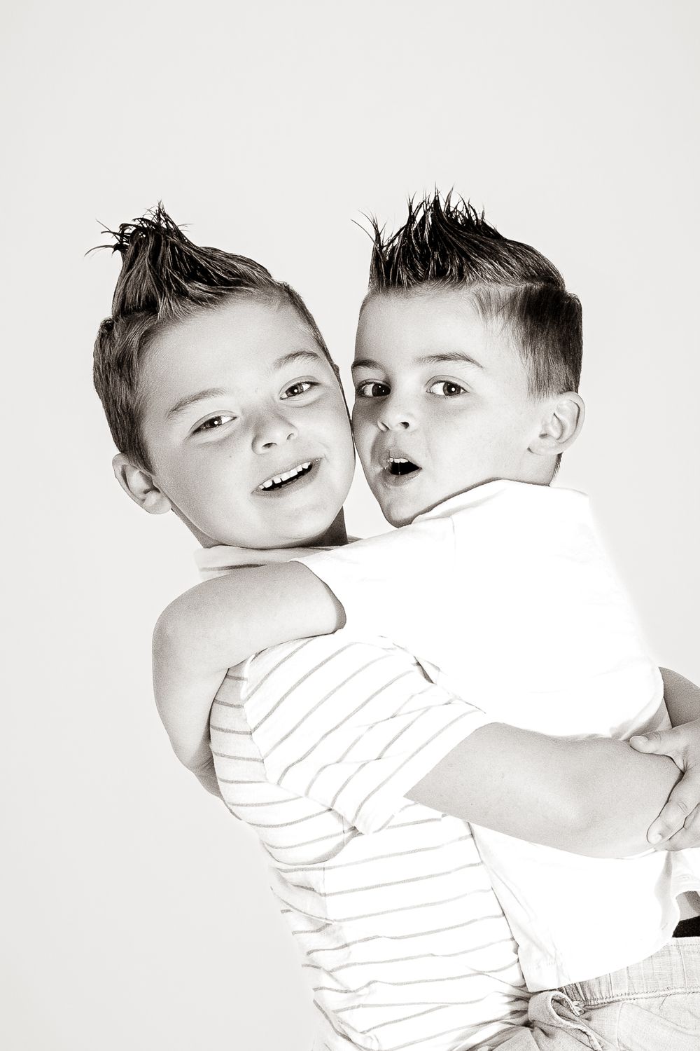 Black and white photo of two young boys with spiked hair hugging and smiling in a studio portrait.