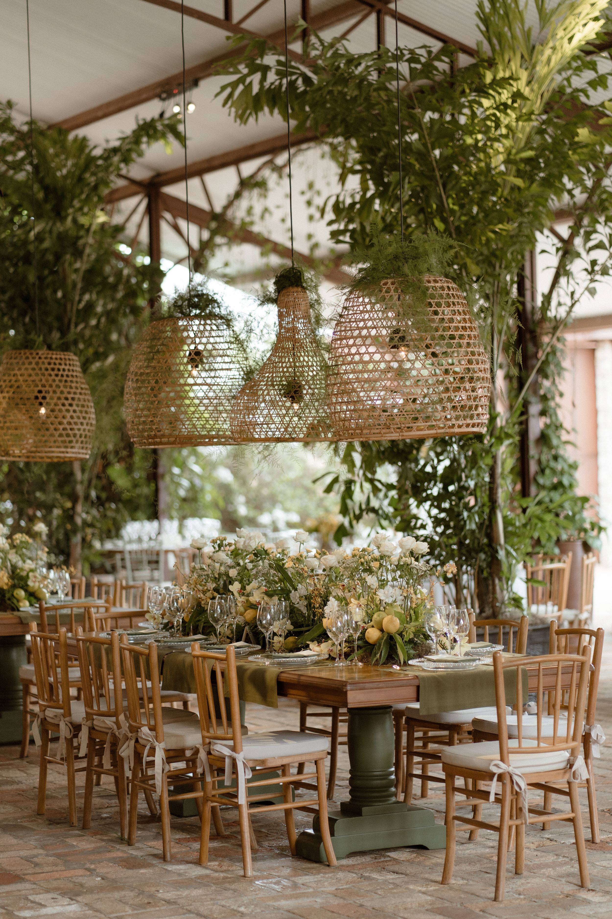 Elegant wedding reception venue with woven rattan pendant lights and wooden chairs arranged under a canopy.