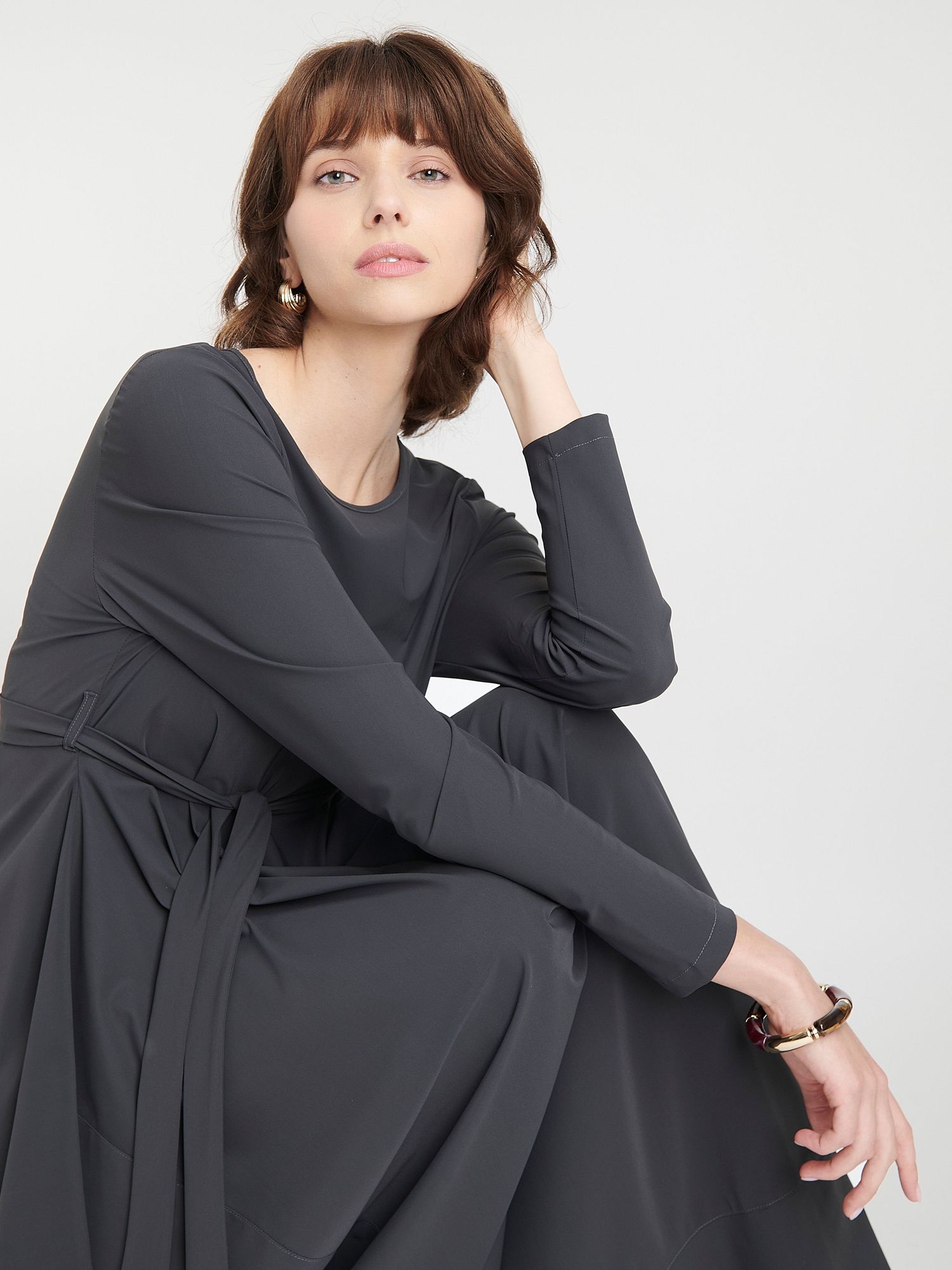 Model wearing black and white geometric patterned turtleneck sweater with black leather shorts against dark background.