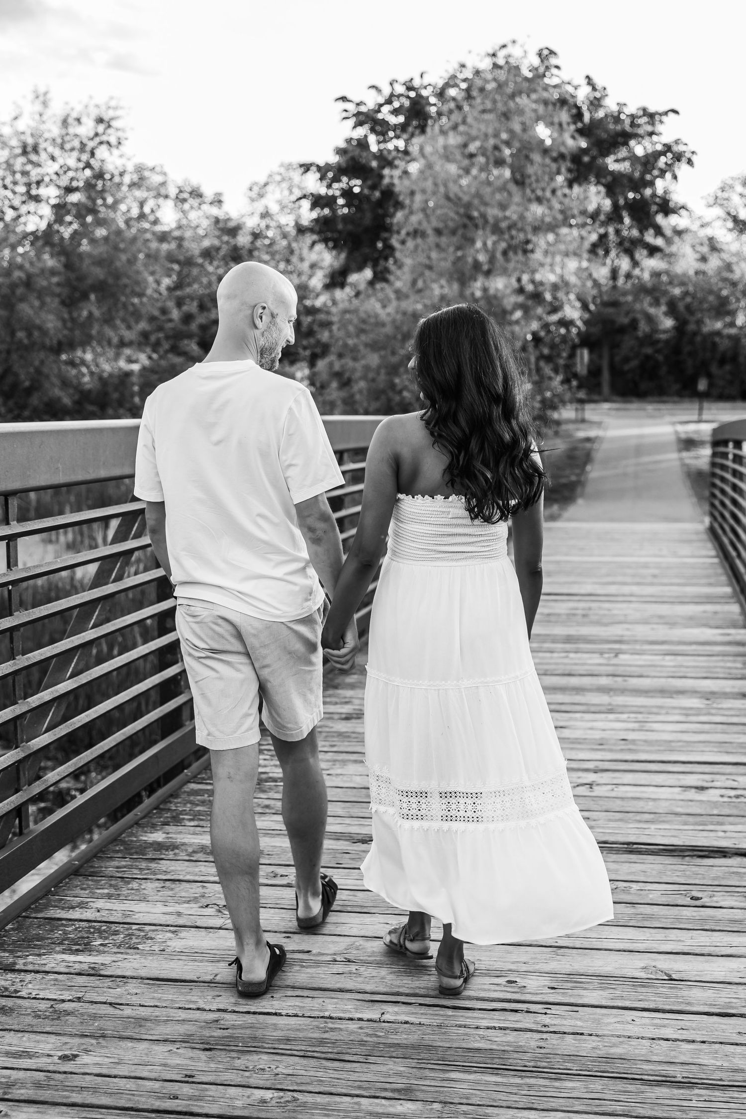 Couple in white outfits walking together on wooden boardwalk during sunset.