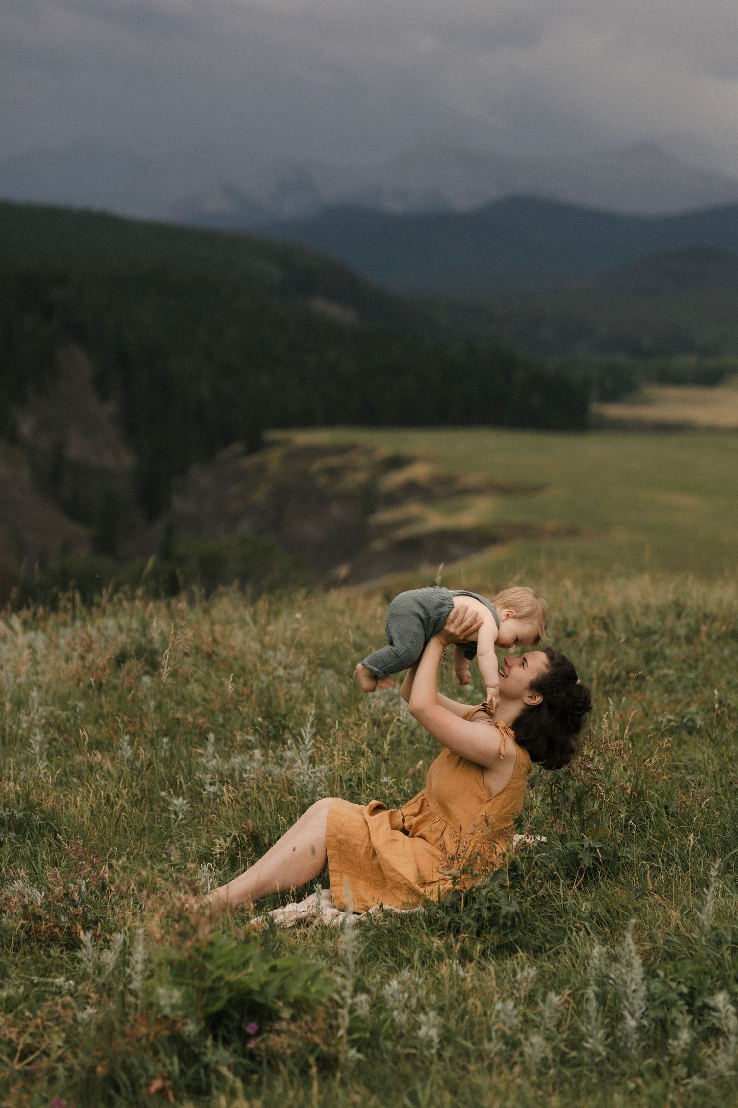 A joyful moment captured in a mountain meadow with rolling hills and stormy skies in the background.