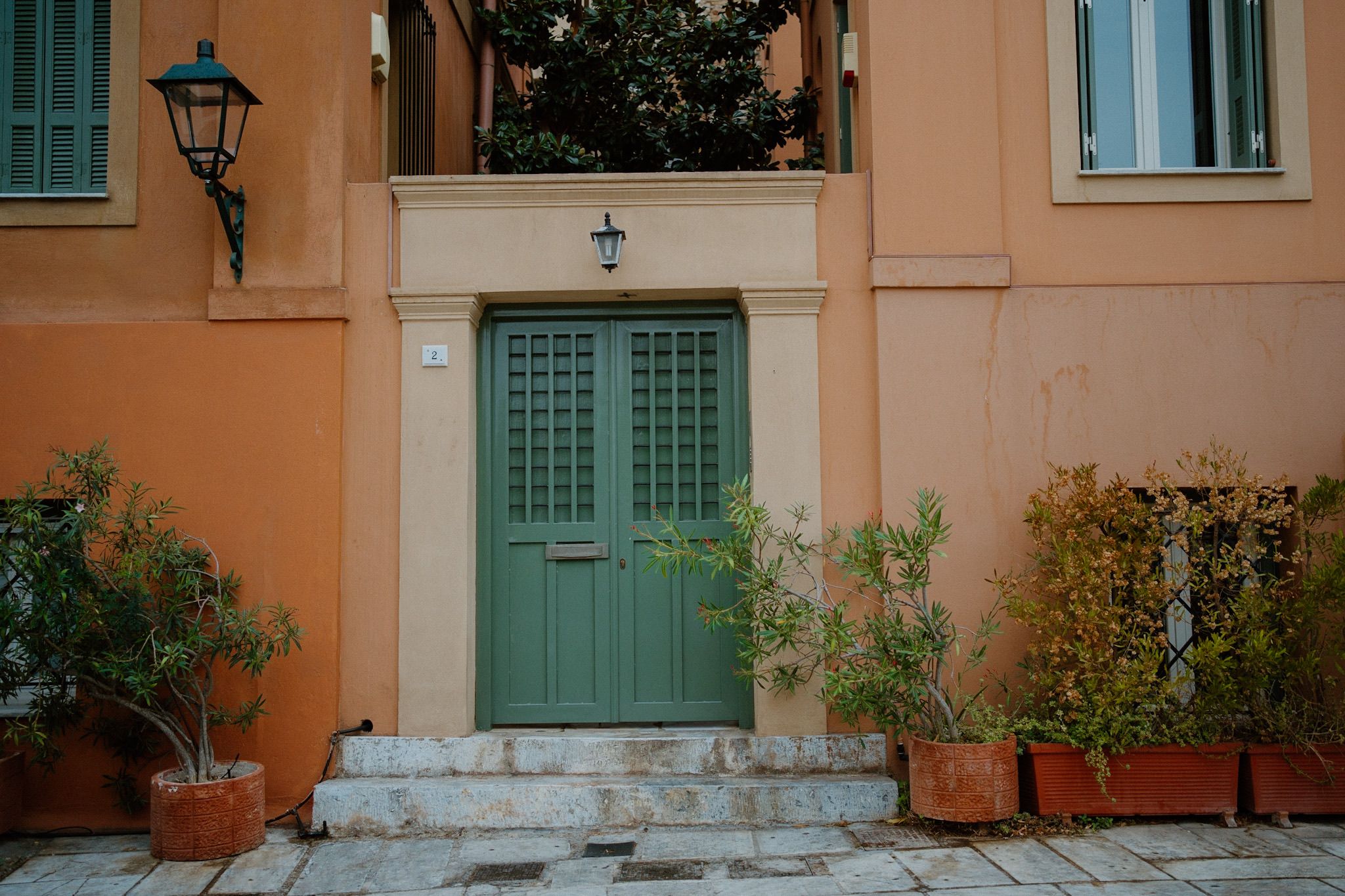 Mint green double doors with white trim on a peach colored building with potted plants and lantern in Athens Greece.