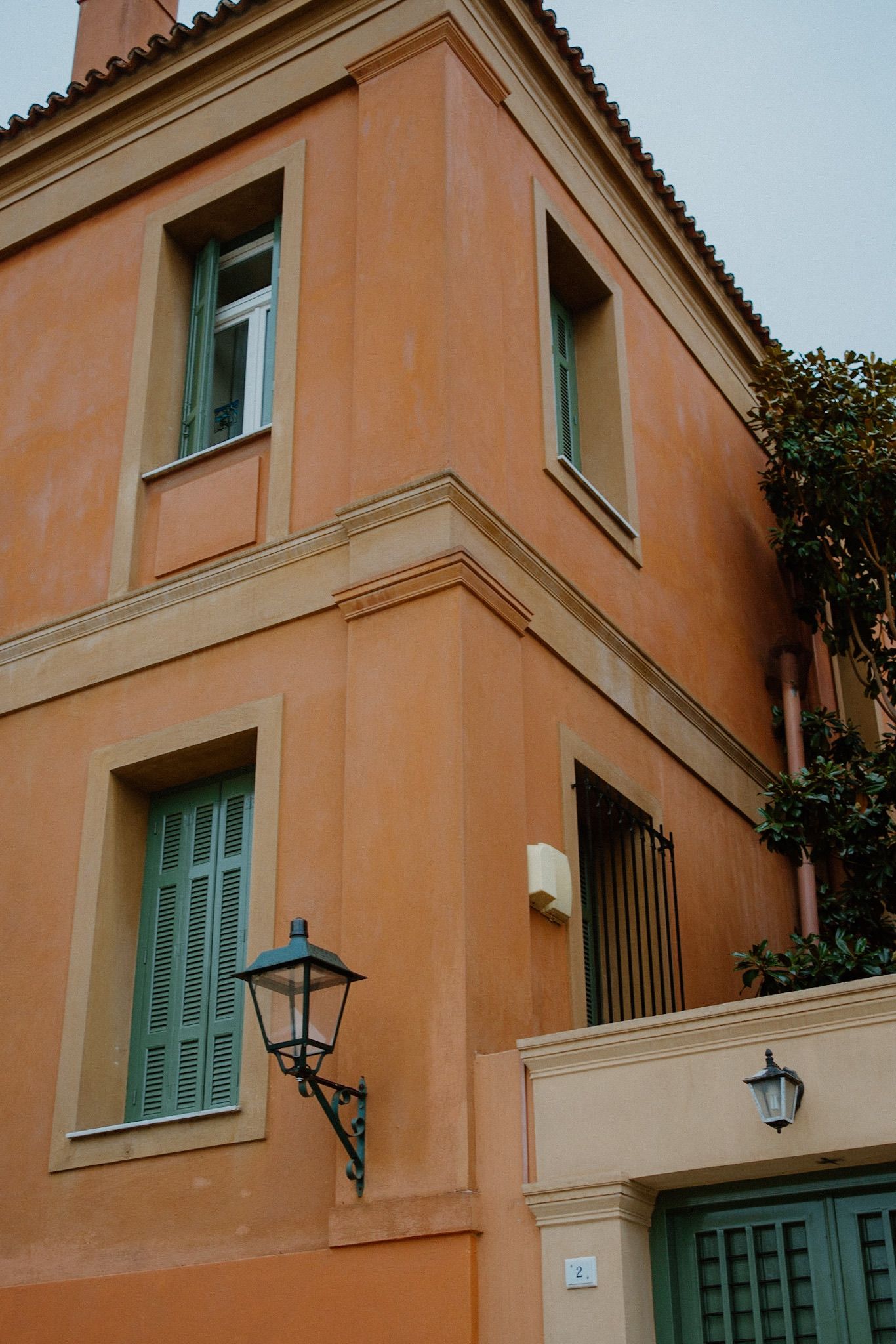 Mediterranean-style building with peach-colored walls, turquoise shutters and decorative lantern-style street lamps.
