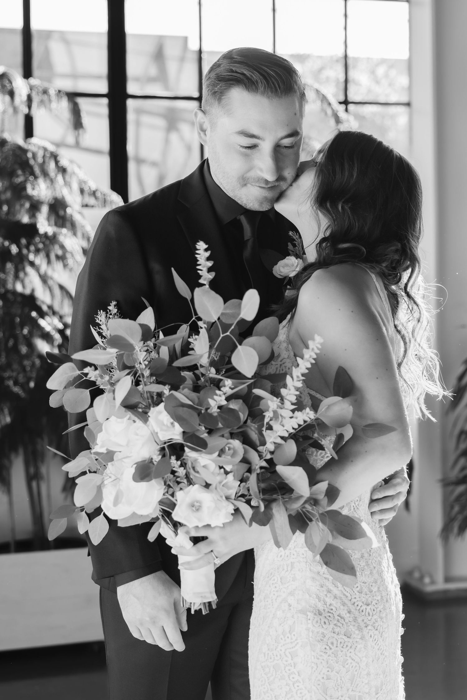 A romantic black and white wedding photo of a couple embracing with a lush floral bouquet featuring eucalyptus and roses.