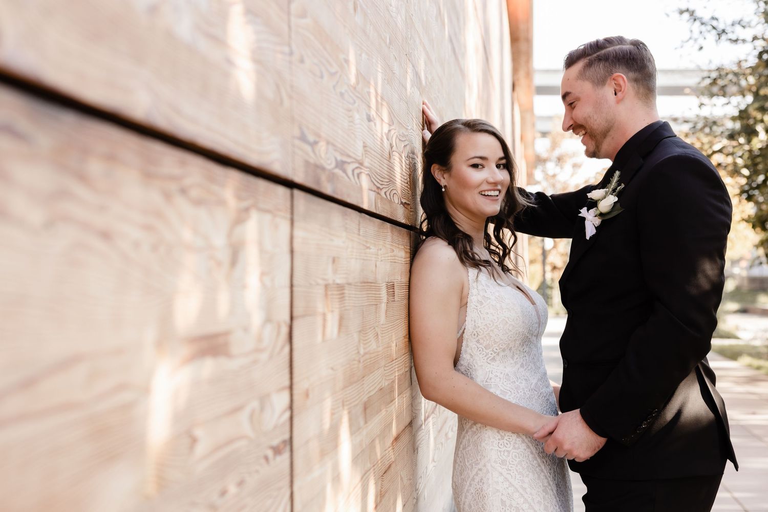A bride and groom share an intimate moment against a sunlit stone wall during their wedding photoshoot.
