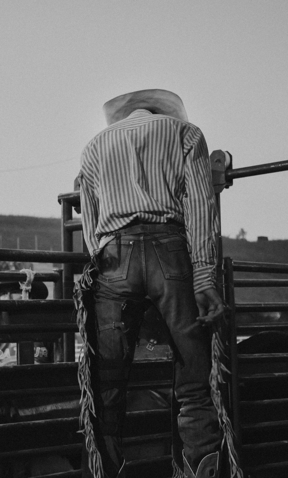 Classic western style with striped shirt and chaps at a rodeo arena.