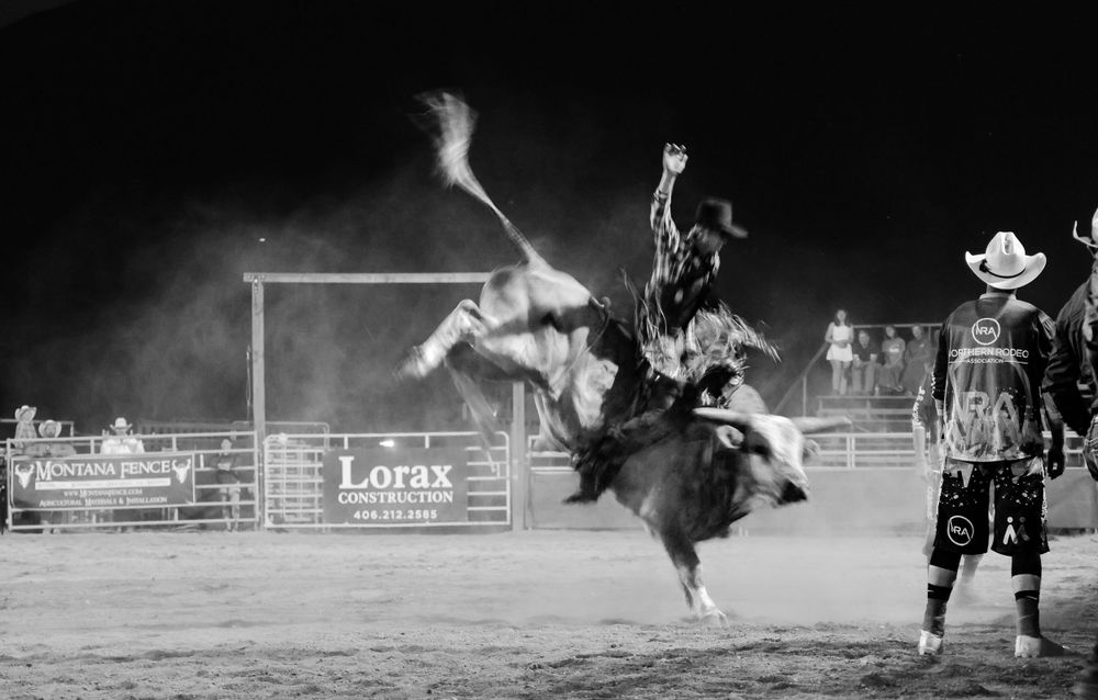 Dramatic black and white shot of bull rider being thrown from bucking bull at night rodeo.