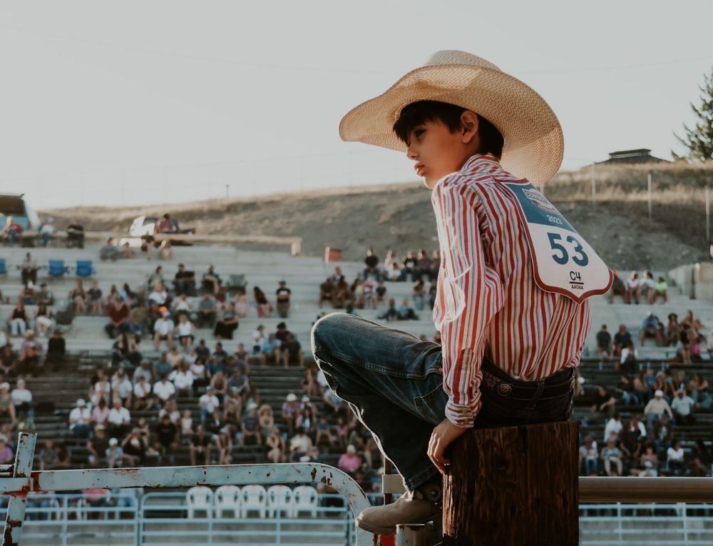 Competitor watches from elevated position at sunset rodeo with crowd in stadium seats.