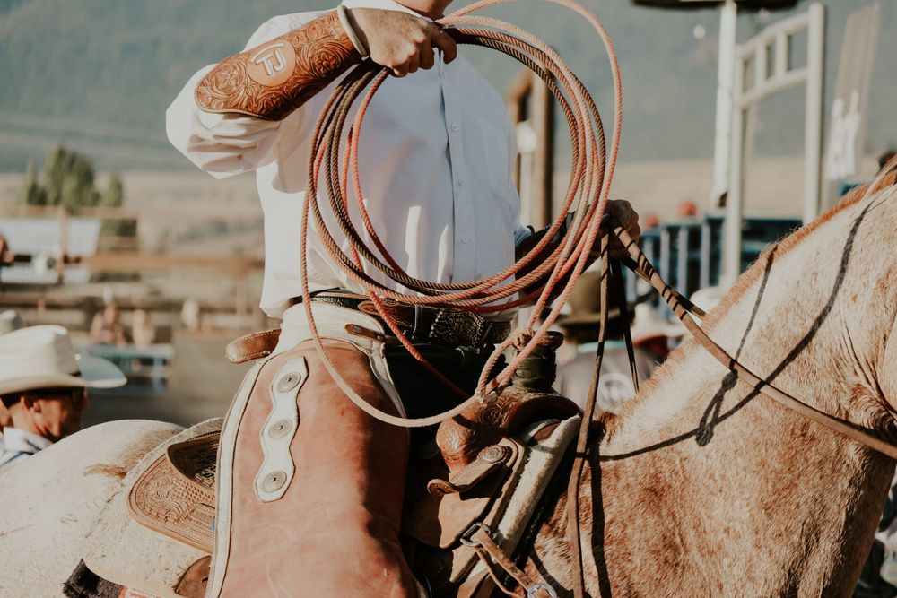 Close-up of western leather saddle with coiled lasso rope on horseback during rodeo event.