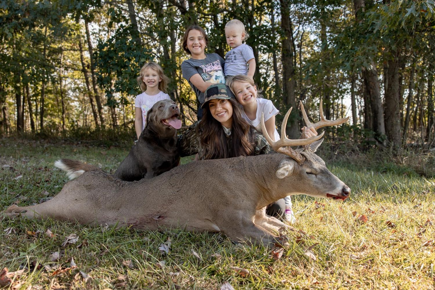 A harvested deer lies on the ground in a wooded area during hunting season.