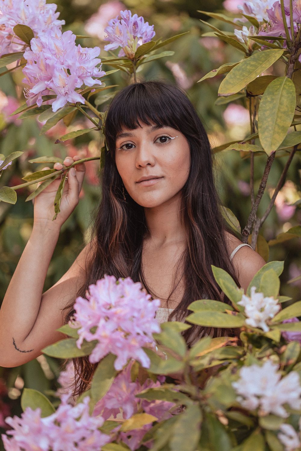 A portrait amidst blooming pink rhododendron flowers and green foliage in soft natural lighting.