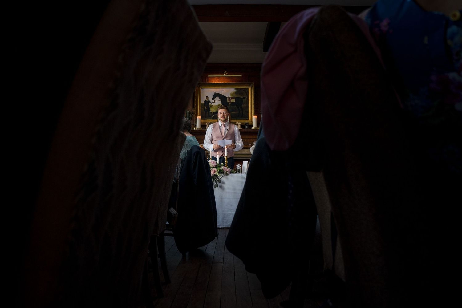 View through wedding guests Wilson Coastal Club wedding venue, Nova Scotia of a wedding speech being performed at the end of a long hall.