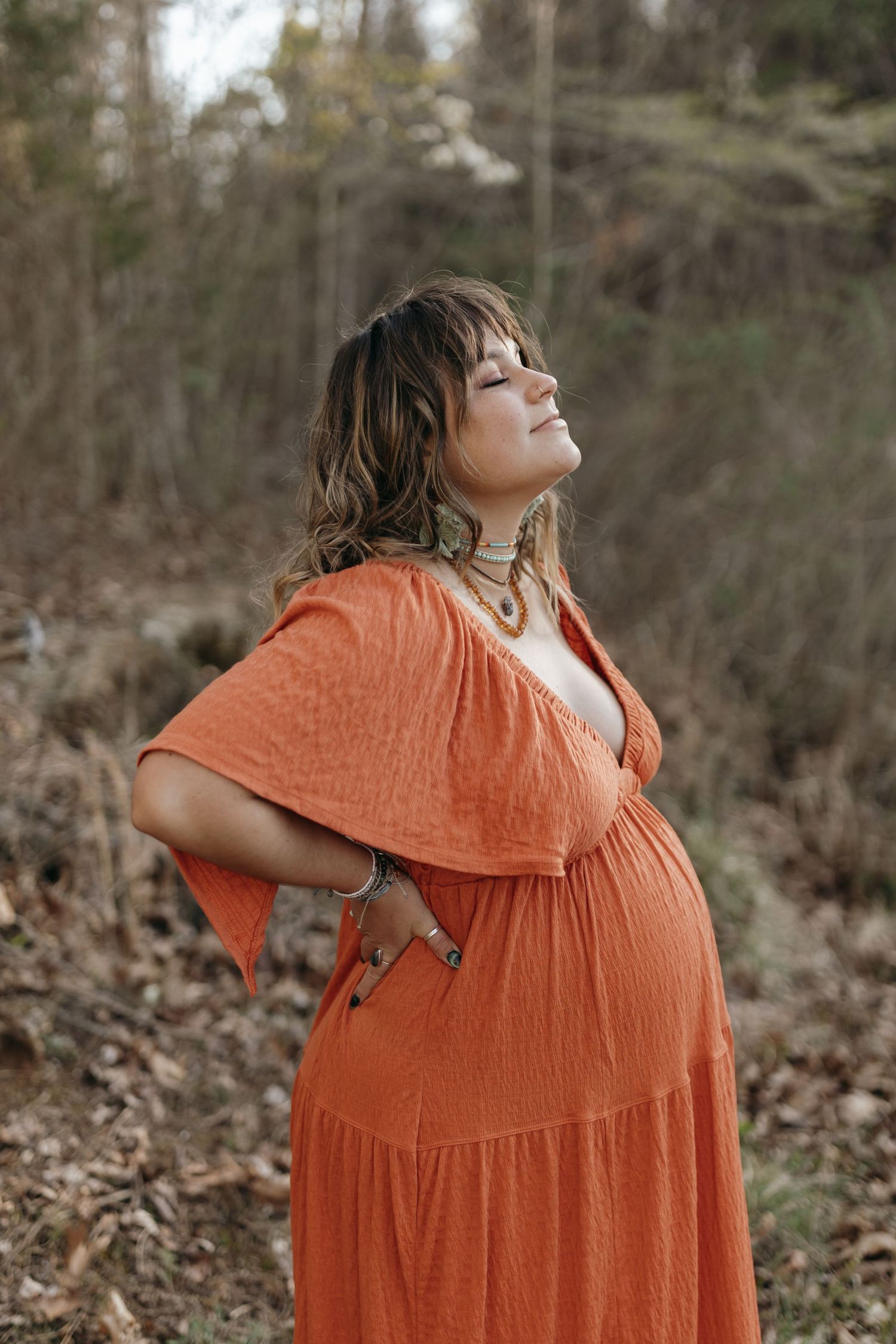 Woman in flowing orange dress poses in nature during golden hour. Virginia/ North Carolina Maternity Session