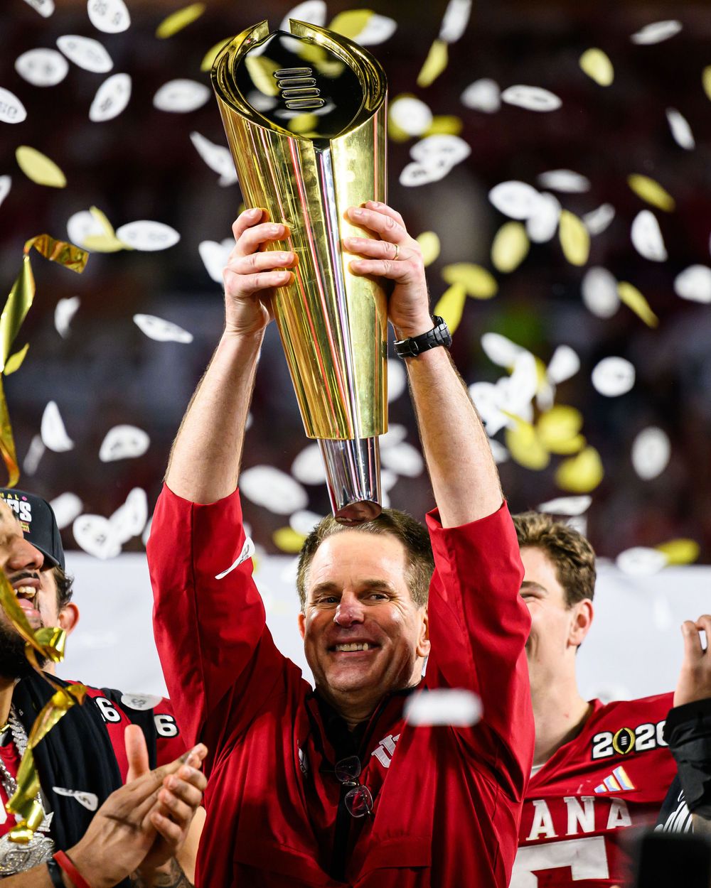 College football championship celebration with trophy being hoisted amid falling confetti at championship game.