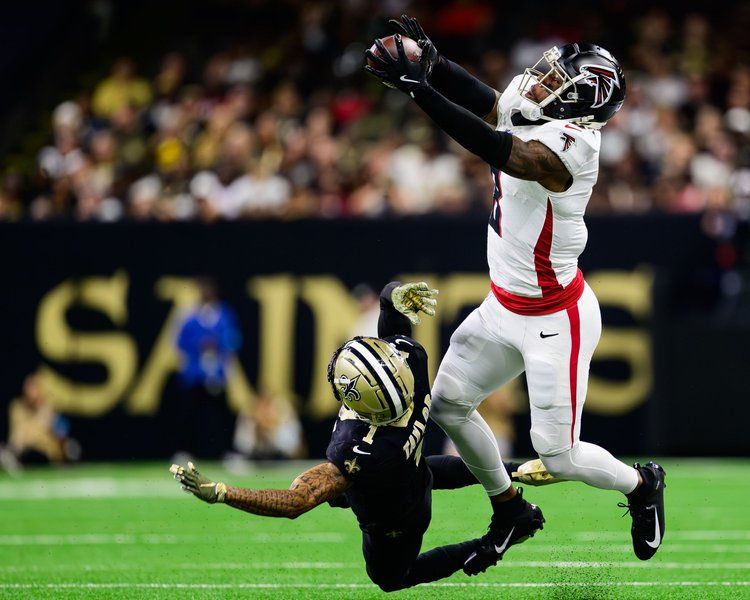 Football players colliding during dramatic catch attempt in NFL game between Falcons and Saints.